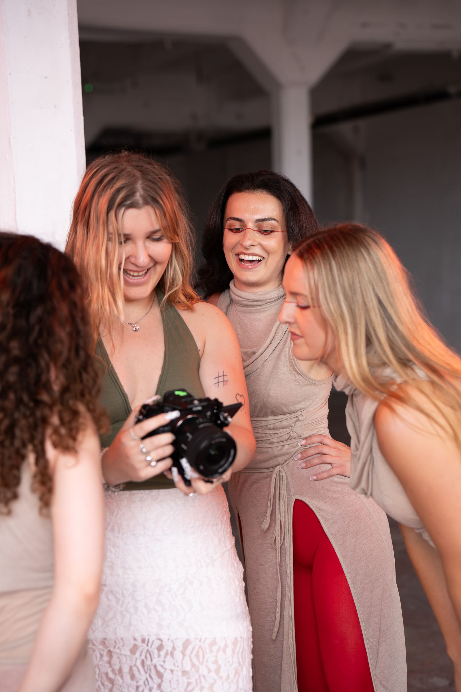 Four women laugh together in a bright studio as one holds a mirrorless camera and shows the others a photo on its screen.