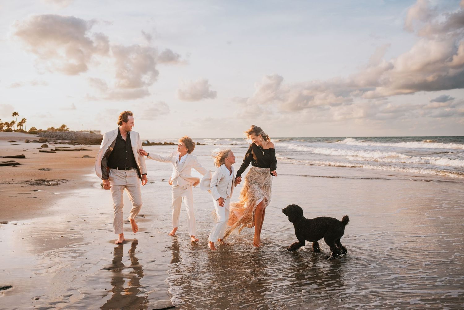 Family with dog playing on beach at sunset, waves in background, casual white outfits, golden hour light during family photos in palm coast