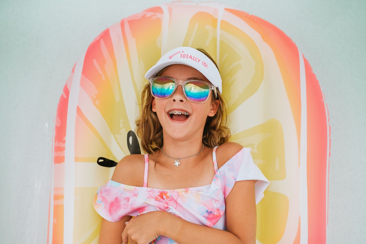 A vacation photoshoot with a smiling girl wearing rainbow sunglasses and visor on a lemon inflatable float at the evermore resort in orlando