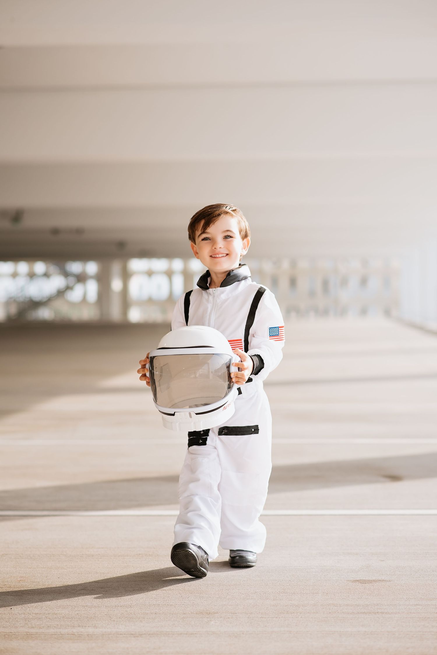 Child portrait session of smiling young boy in white astronaut costume holding a space helmet in orlando Florida