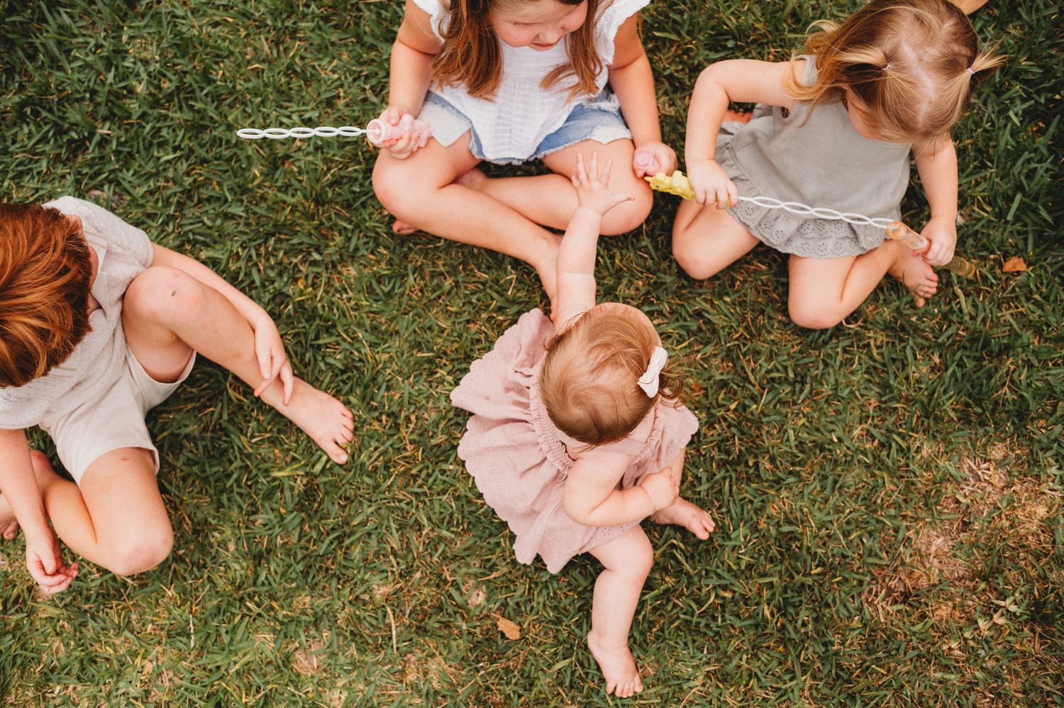 Four young children sitting on green grass outdoors, including a baby in a pink tutu dress during an in-home family photoshoot in central fl
