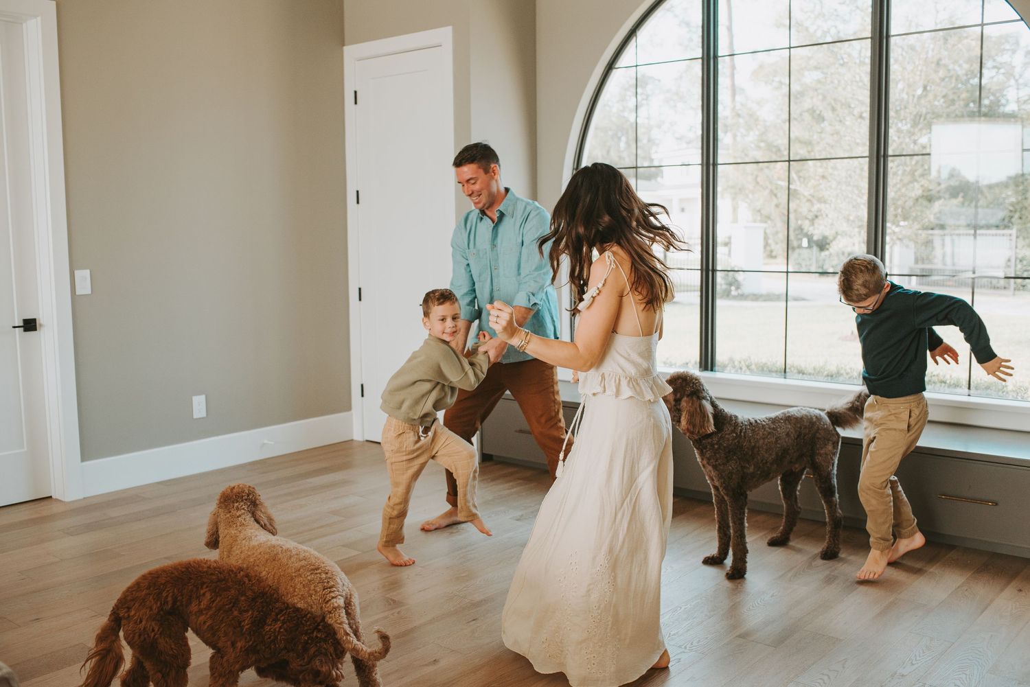 Family dancing with two dogs in a bright modern home with hardwood floors and large arched window during an in-home photoshoot in orlando fl