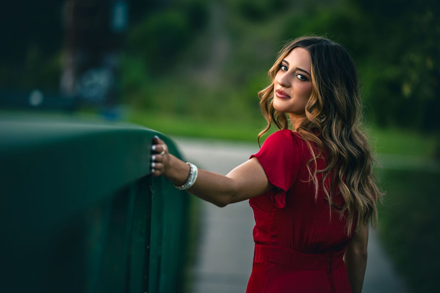 Portrait in red dress reaching for railing during sunset.
