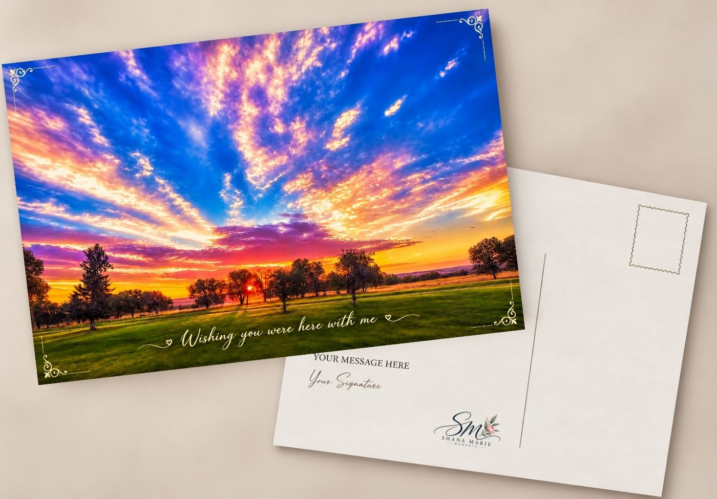 Sunset landscape postcard with vibrant orange and blue sky, green fields, trees, and cursive text reading Wishing you were here with me.