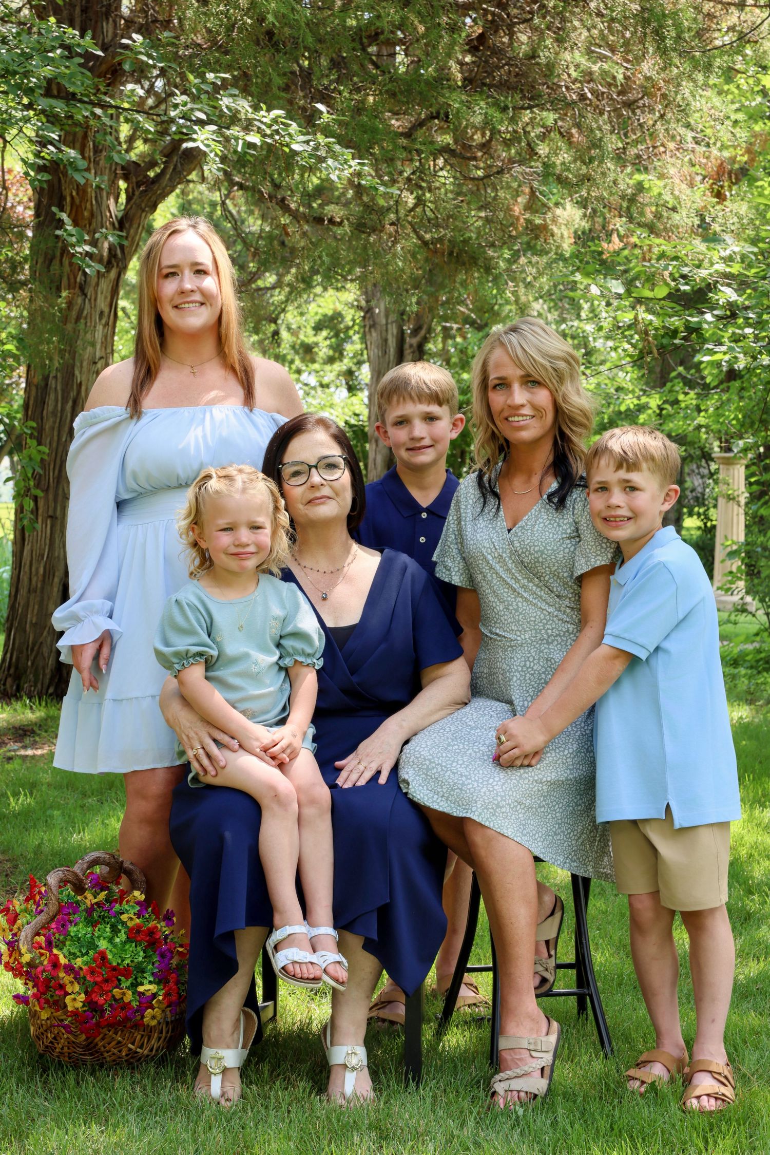 Family portrait of two women with three children smiling outdoors in a lush green garden setting.