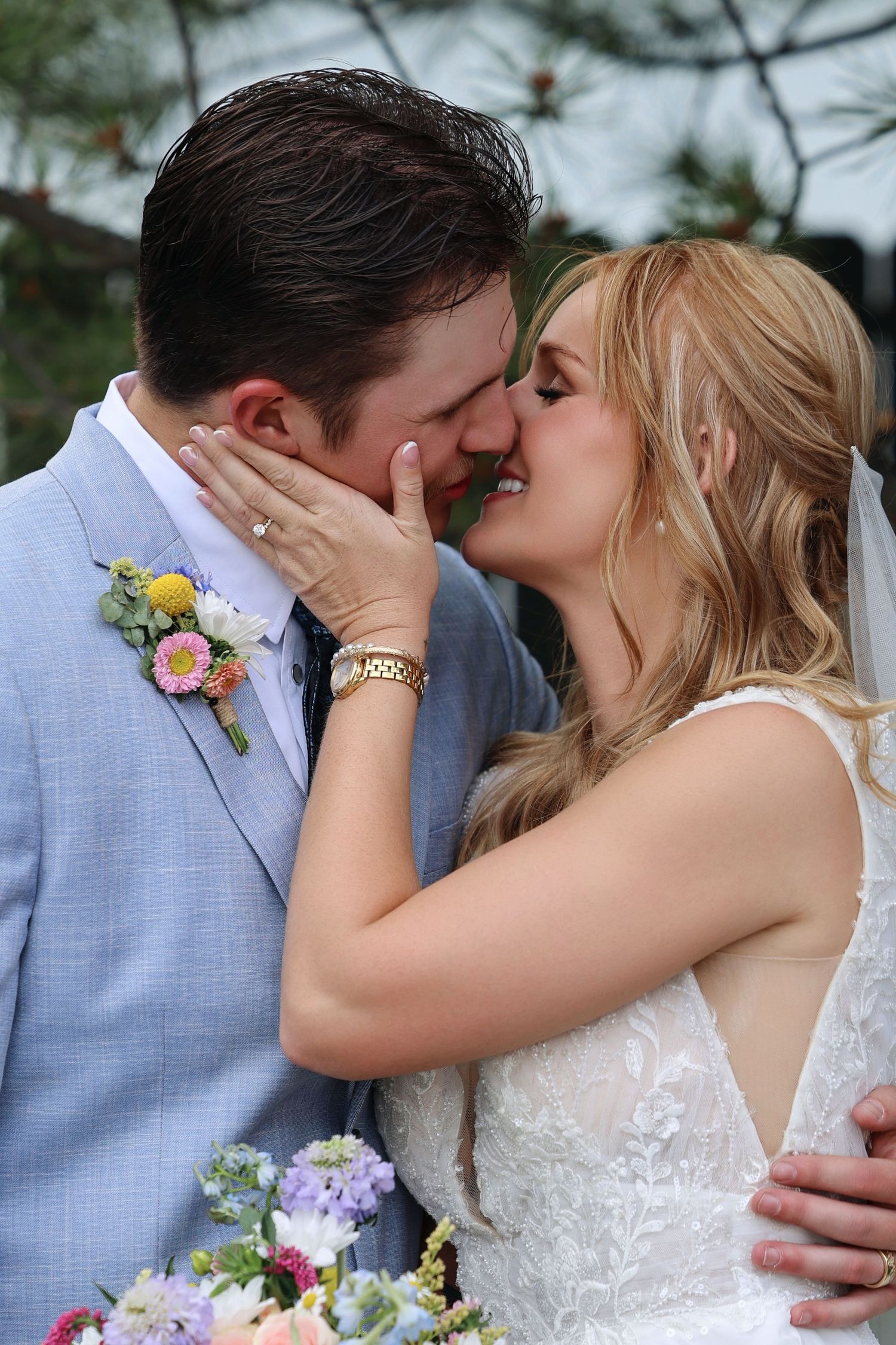 Bride and groom share their first kiss, with colorful floral boutonniere and wedding bouquet visible.