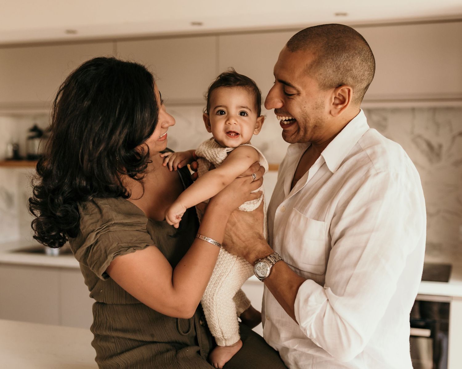 Happy young family with mother, father, and baby smiling together in a bright modern kitchen.