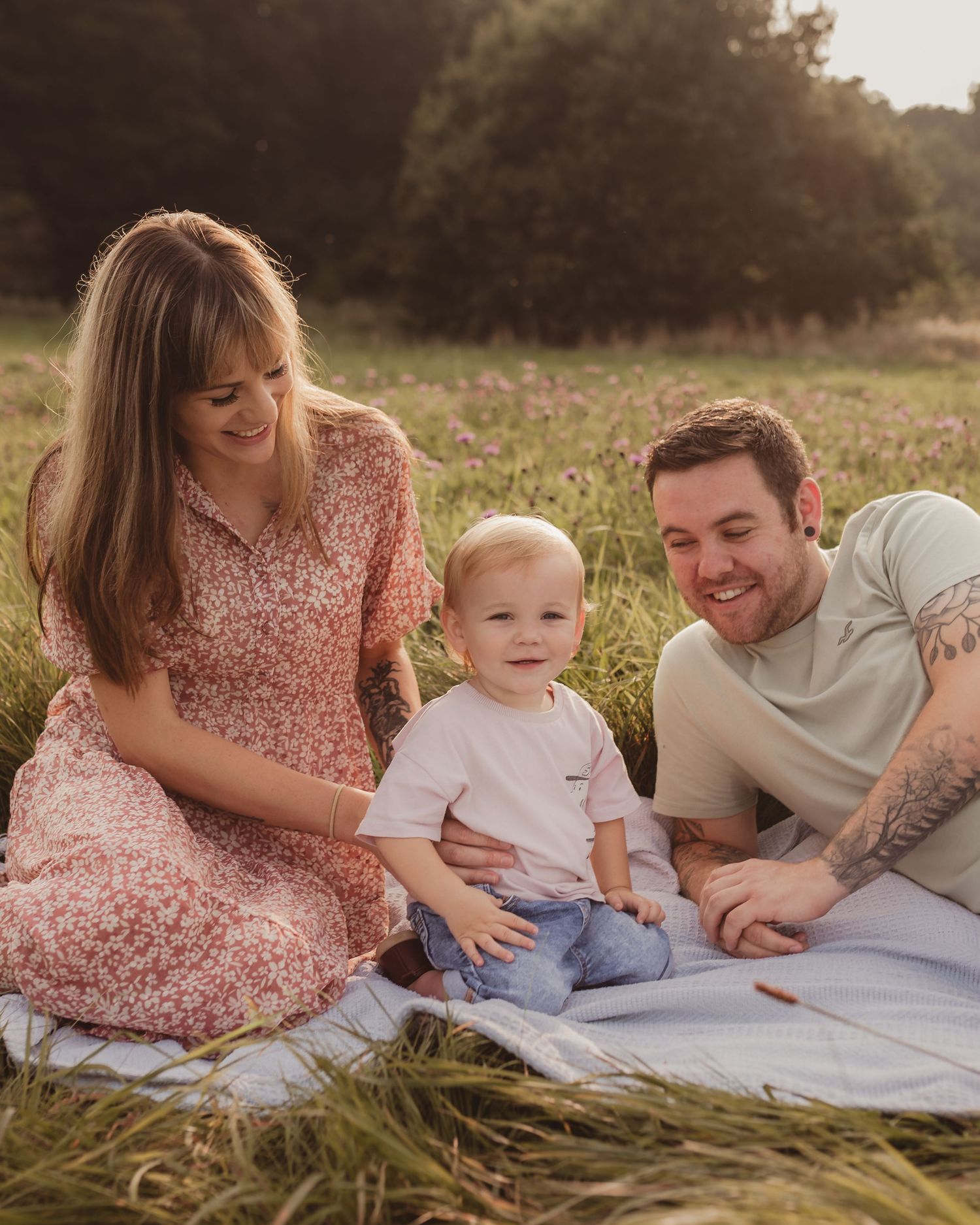 Young family of three sitting on a blanket in a wildflower meadow during golden hour sunset.