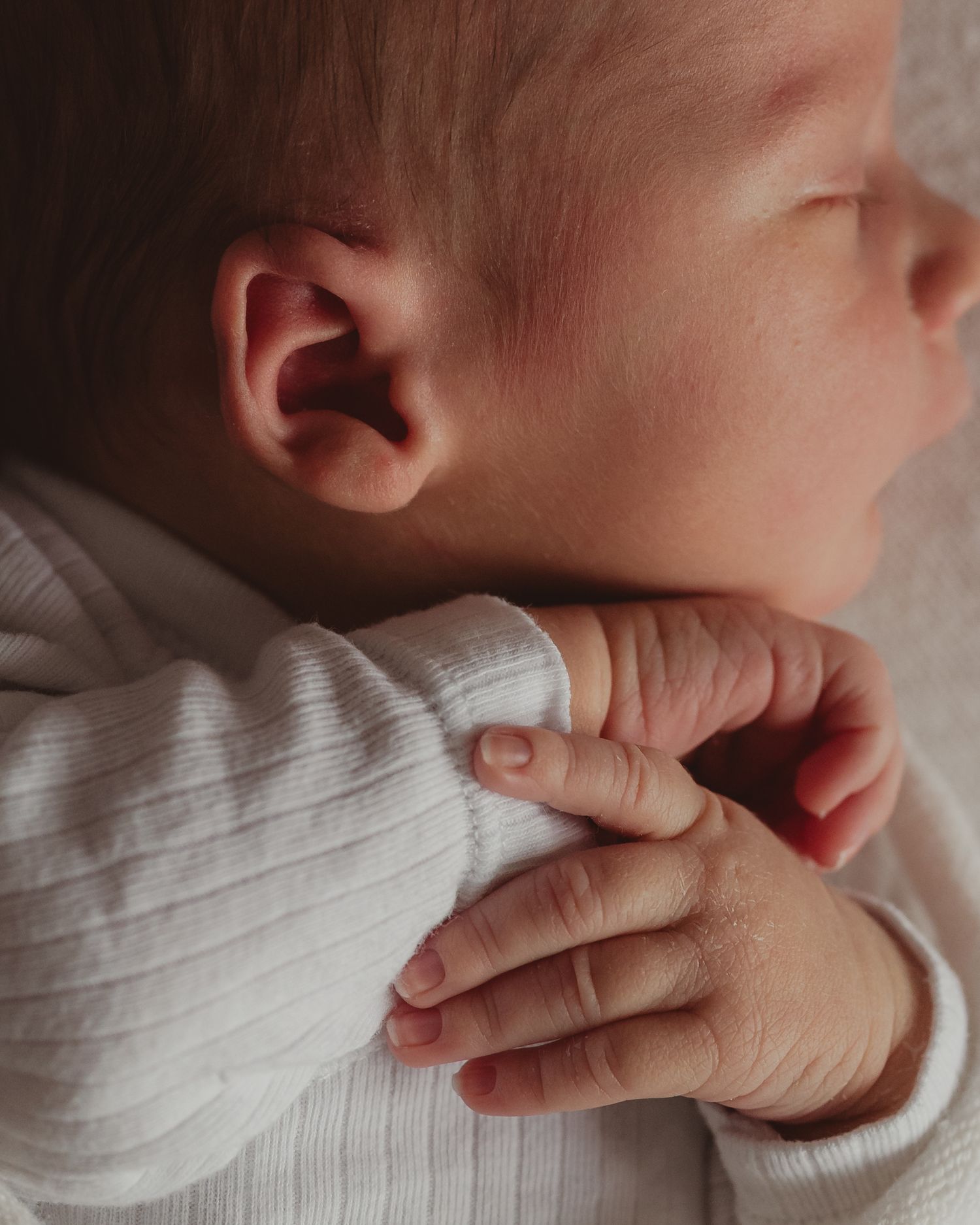 Close-up of a sleeping newborn baby in a white outfit with tiny fingers curled gently.