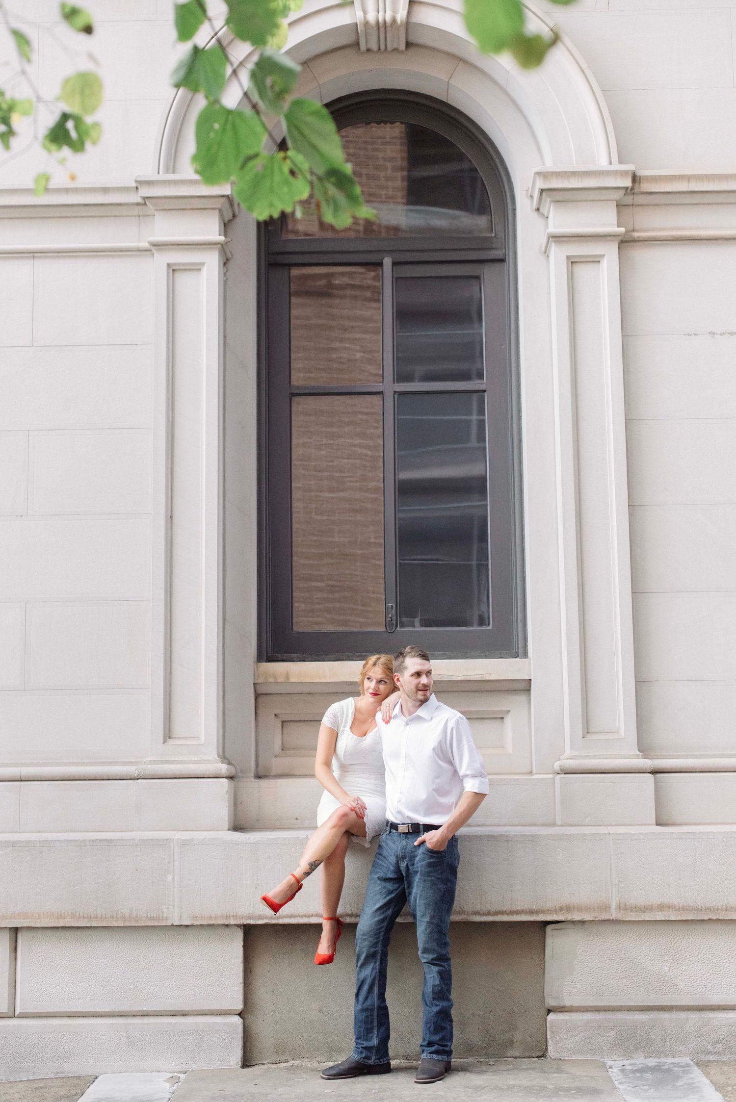 Romantic couple posing against a white stone building with arched windows.