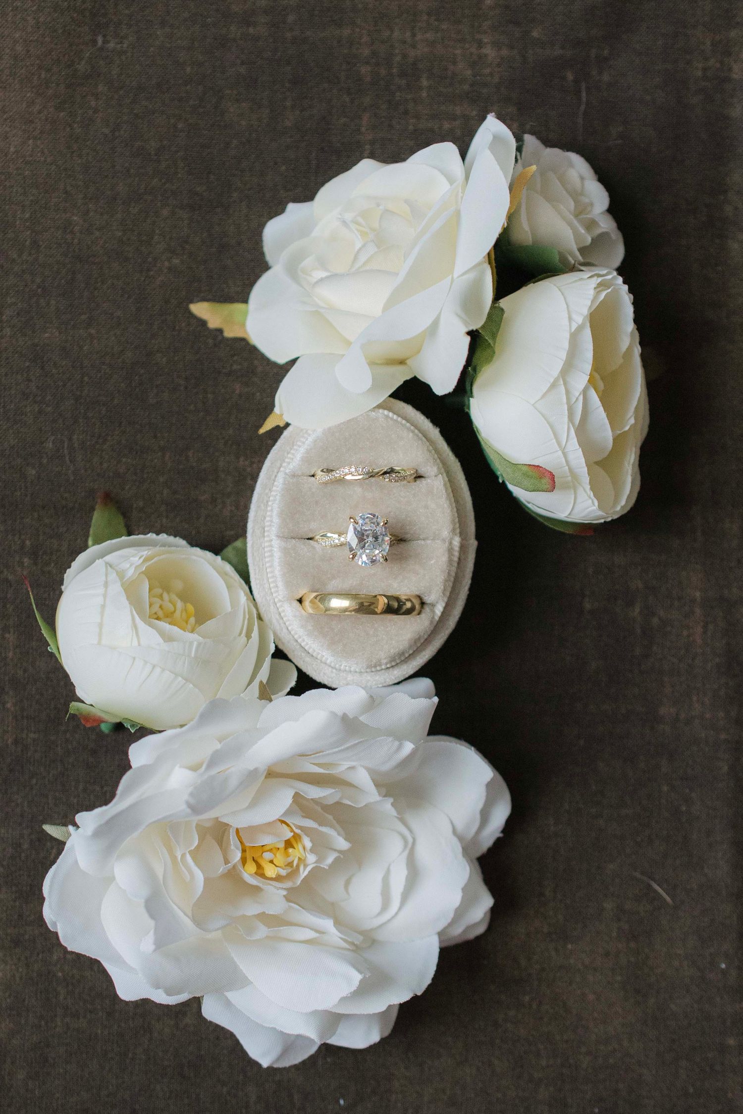 White wedding rings nestled among delicate white roses against a dark background.