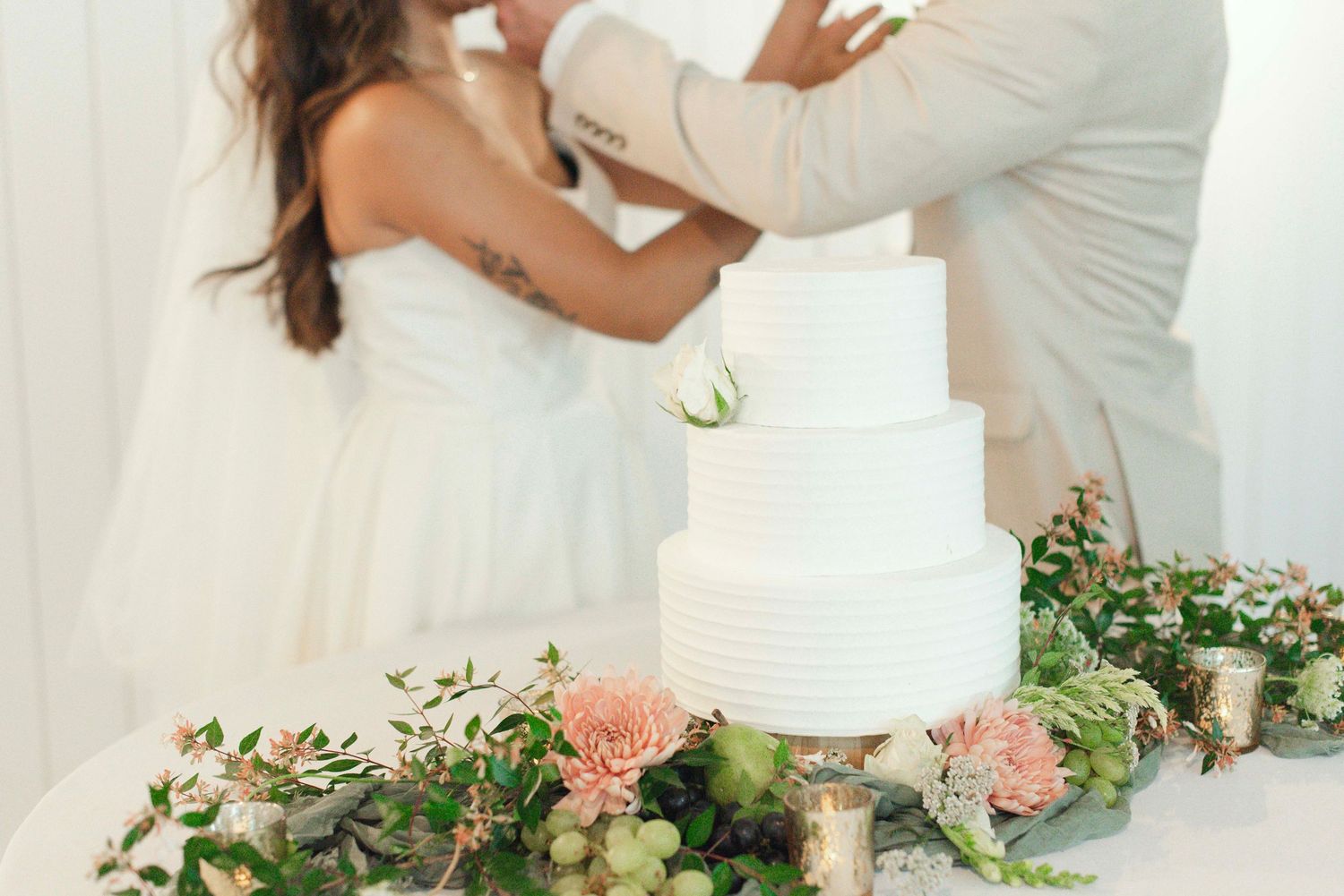 A romantic couple embraces at an outdoor wedding ceremony decorated with delicate floral arrangements and greenery.