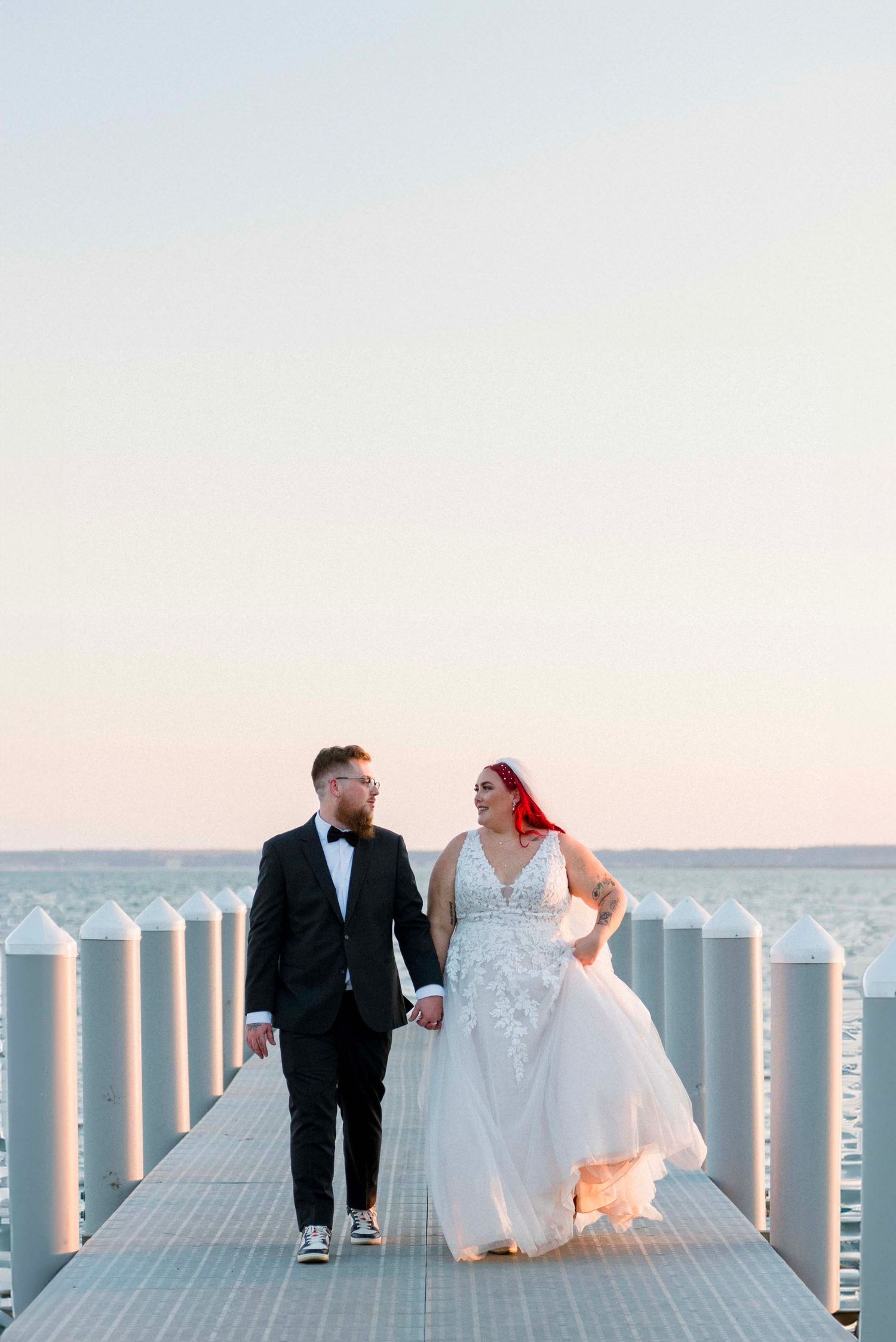 Sunset wedding photos on a waterfront dock with white posts silhouetted against the sky.