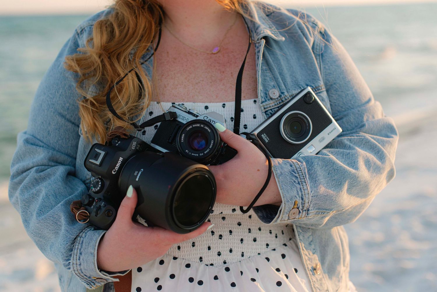 Person holding vintage cameras wearing polka dot dress on beach.