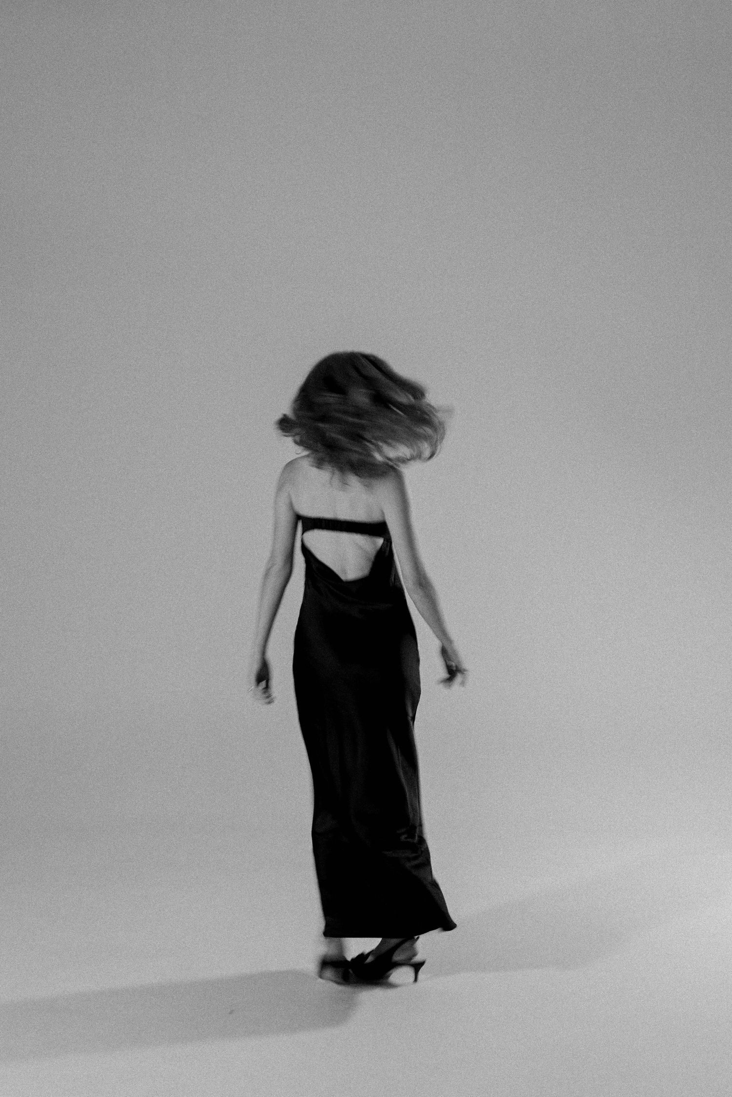 Figure in black dress moving expressively against minimalist grey background.