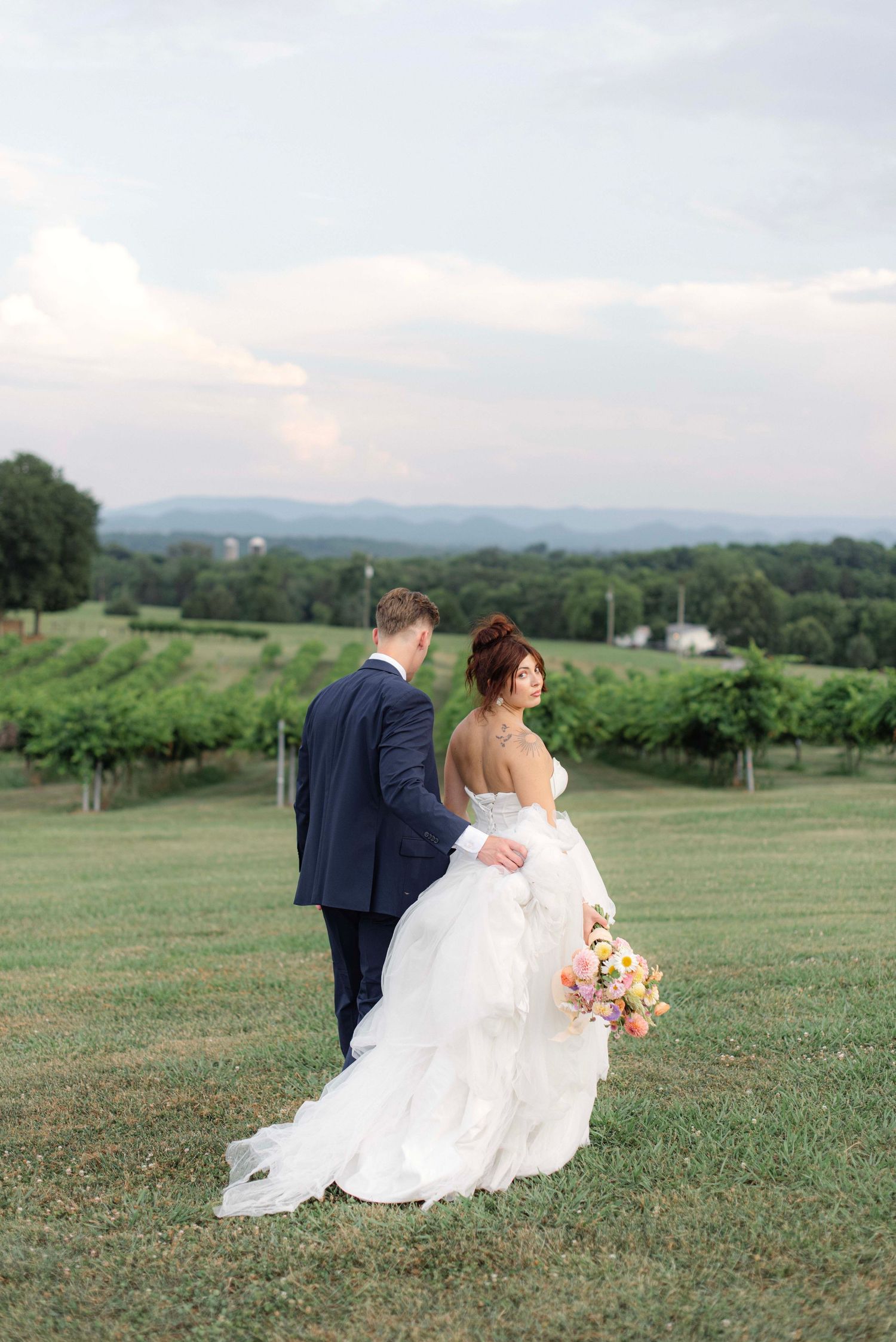 A romantic wedding couple walks through a scenic hillside meadow with flowing white dress and suit.