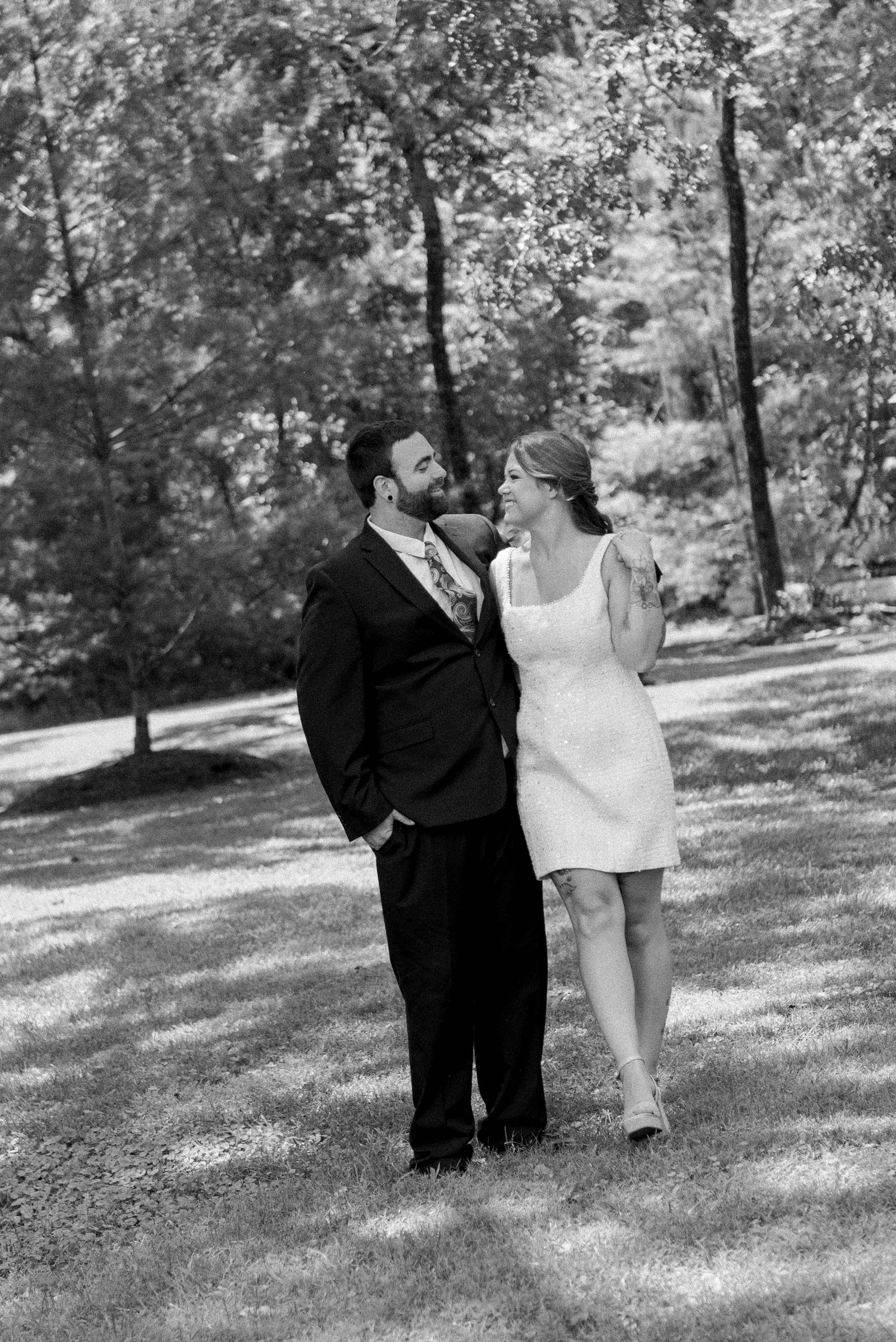 A couple in formal attire walks together through a sunlit park in a series of black and white photographs.