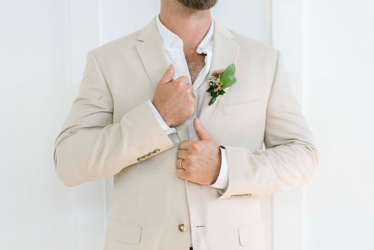 A person wearing a light beige suit adjusts their tie while standing against a white background.