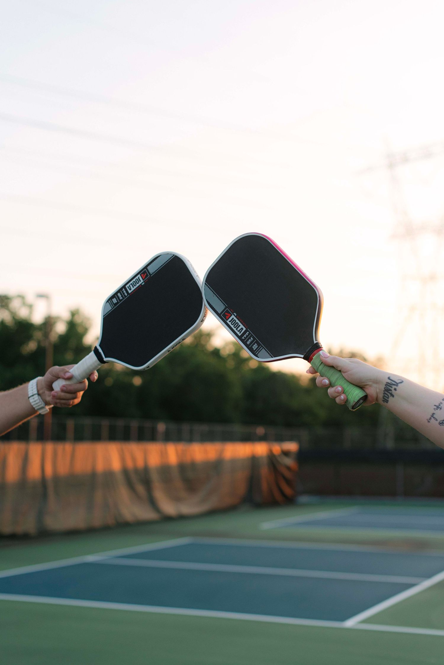 Tennis player serving ball on outdoor court at sunset with dramatic lighting and shadows.