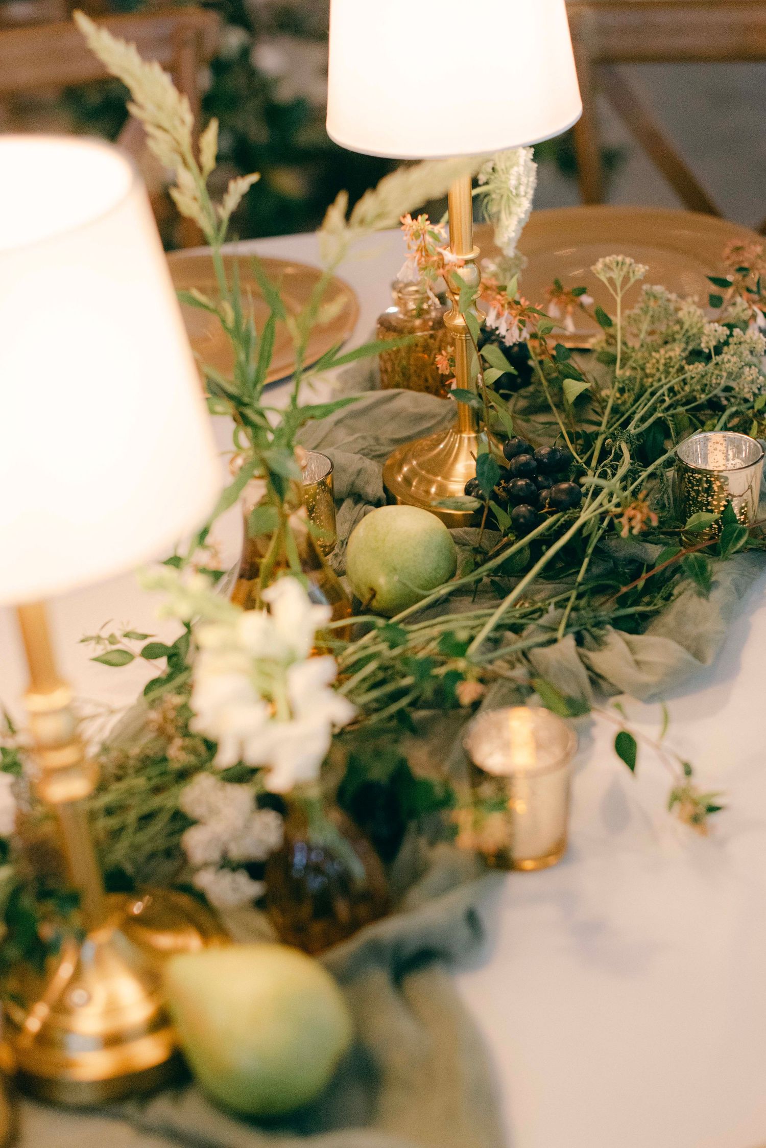 Wedding table decor with delicate floral arrangements, greenery, and gold accents under soft lighting.