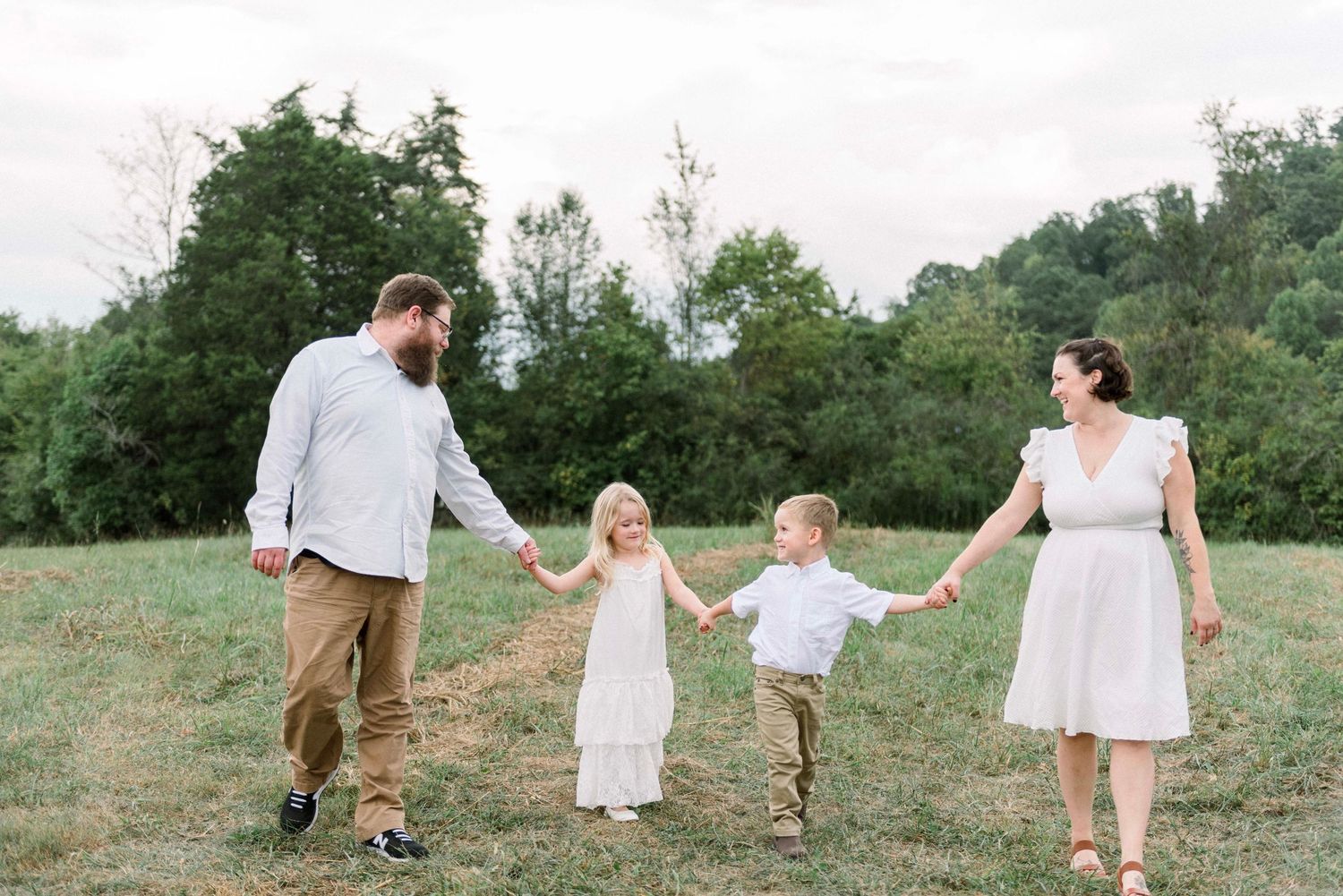Family holding hands walking together through a grassy field.