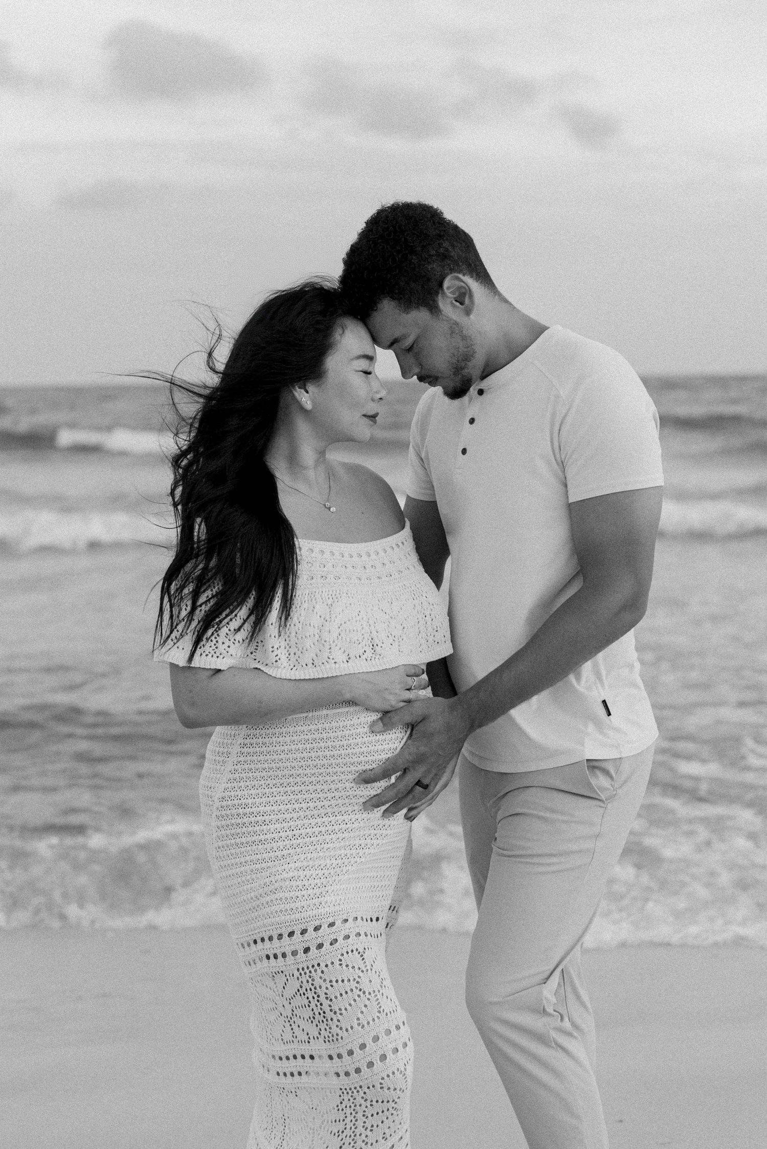 A romantic black and white beach maternity photo with a couple embracing by the ocean waves.
