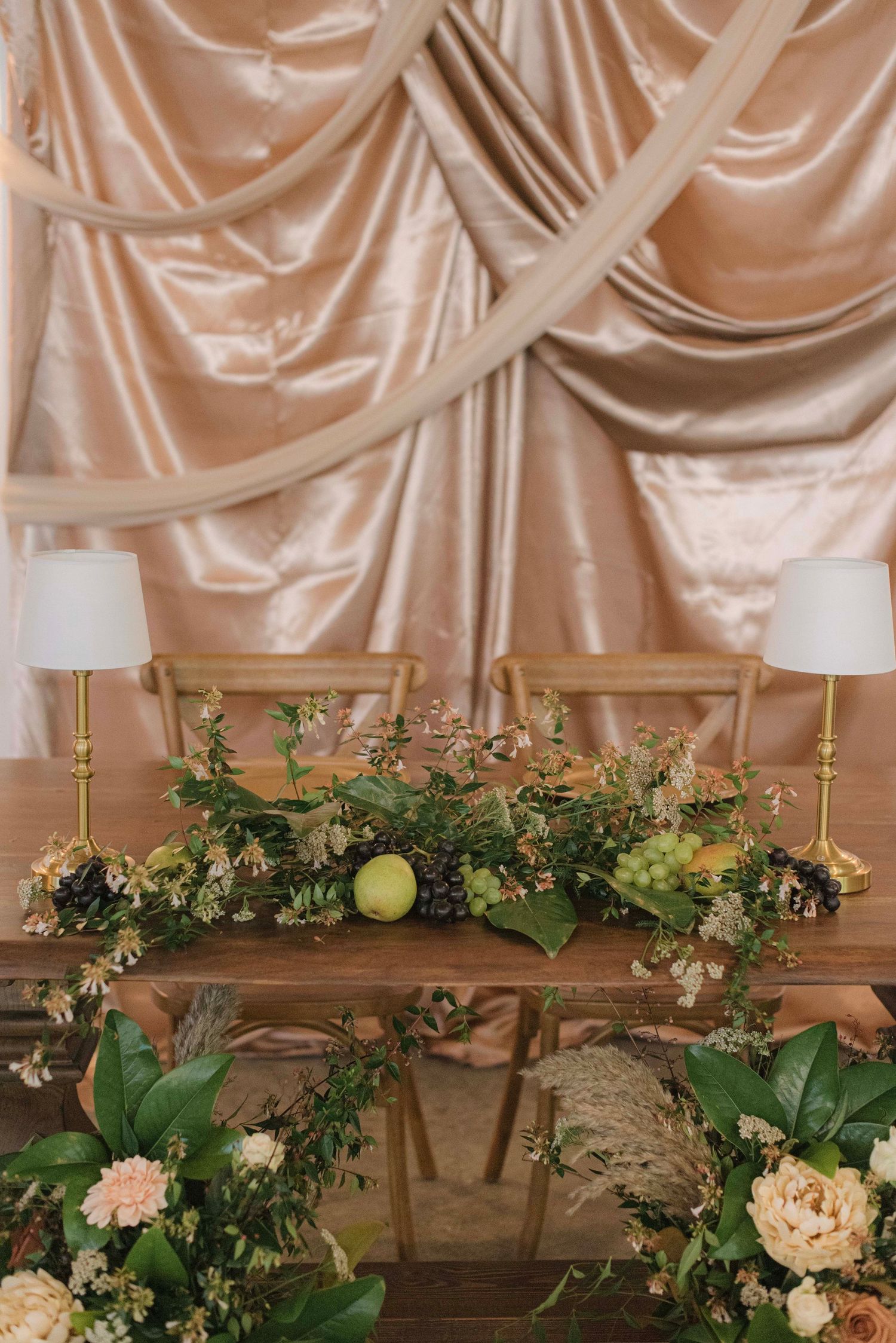 Elegant table display with floral arrangements, white lamps, and draped champagne-colored satin backdrop.