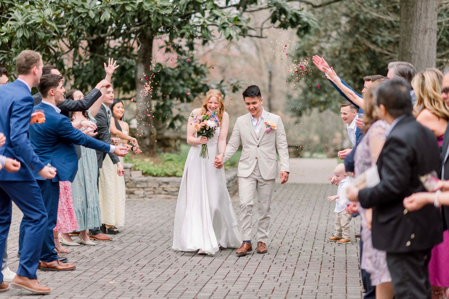 Wedding party and guests celebrating on a stone pathway surrounded by gardens.