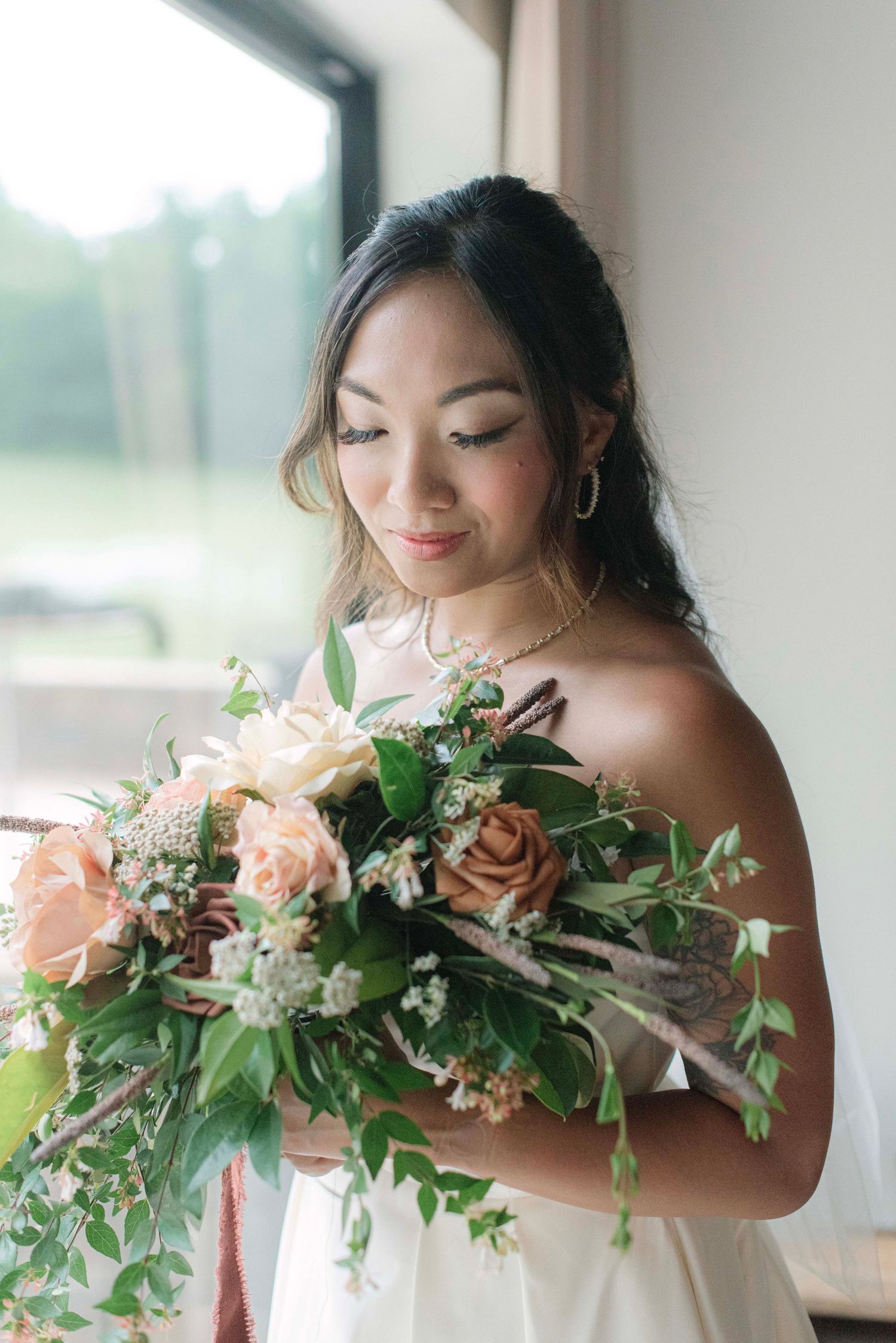 A bride holds a lush peach and blush wedding bouquet with cascading greenery in a series of romantic portraits.