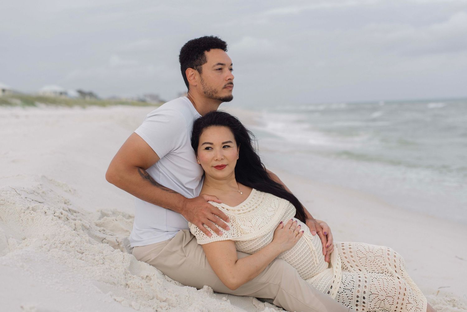 A couple embraces on a white sandy beach with ocean waves in the background.
