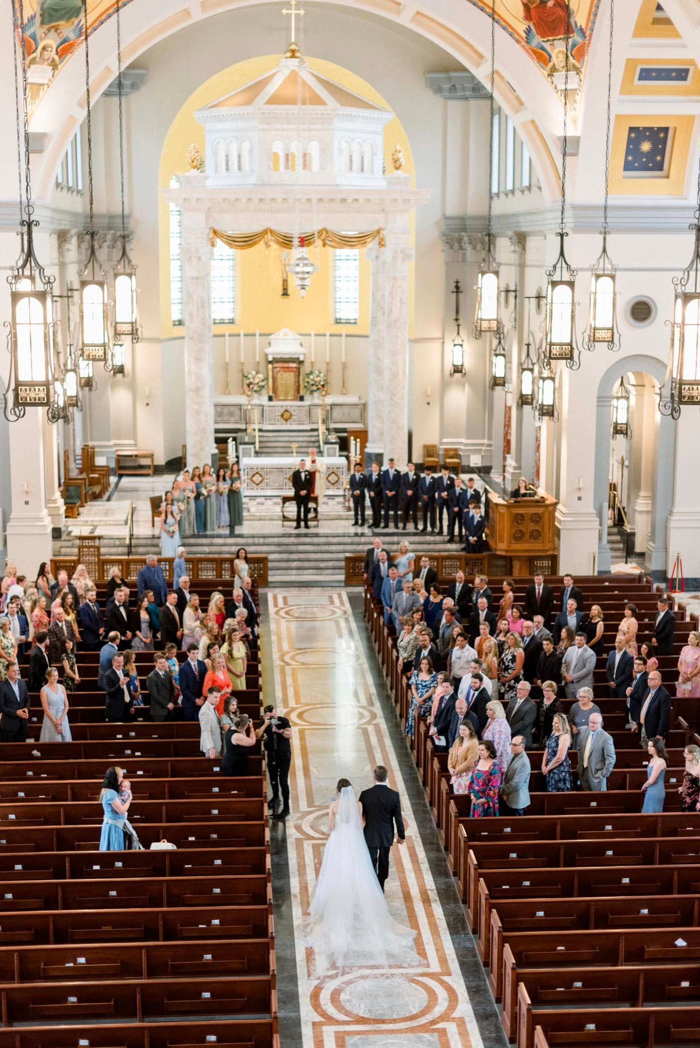 A traditional church wedding ceremony with guests seated in wooden pews as the couple walks down the ornate aisle.