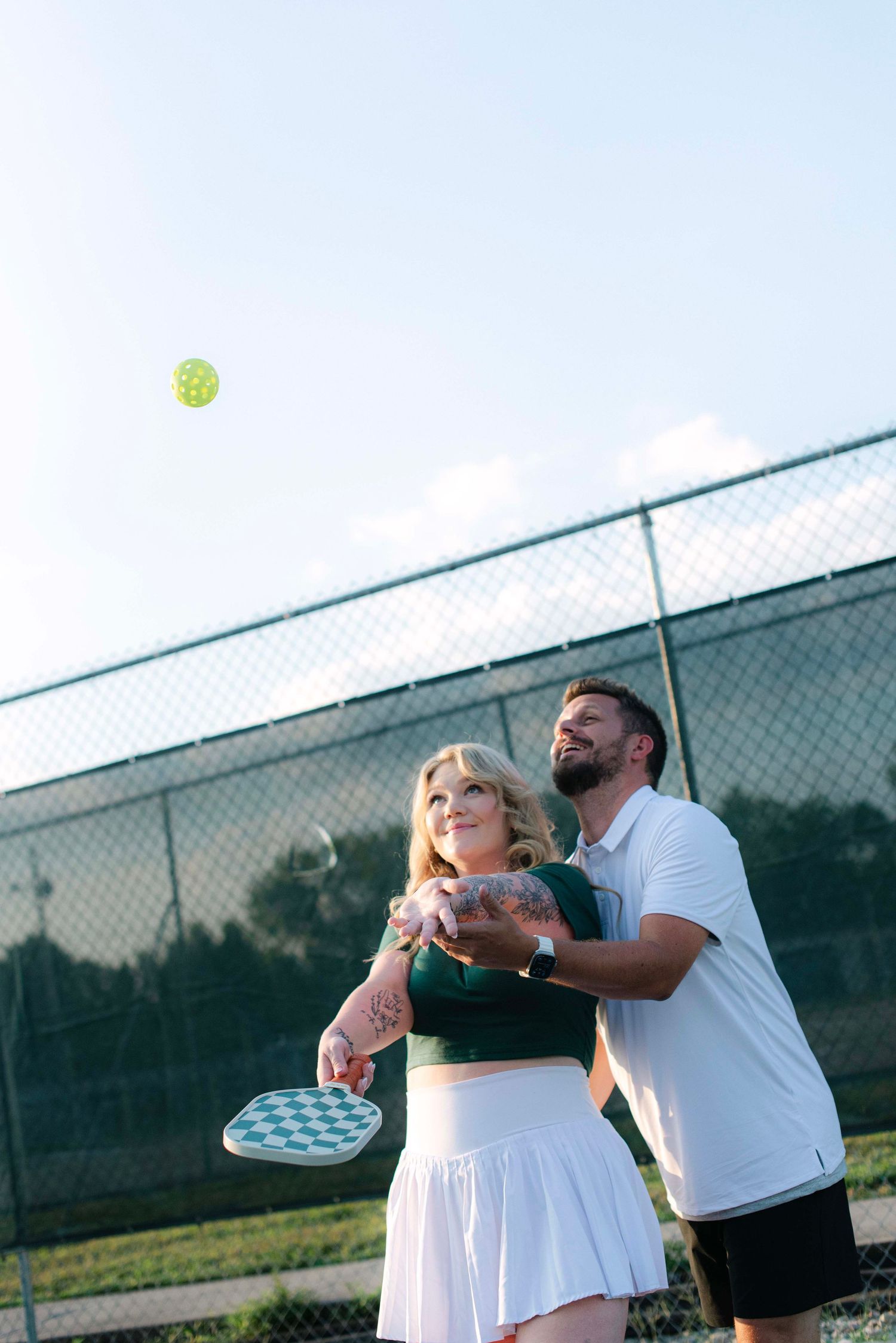 A sequence of tennis serve motion shots showing a player in white hitting a tennis ball on an outdoor court.