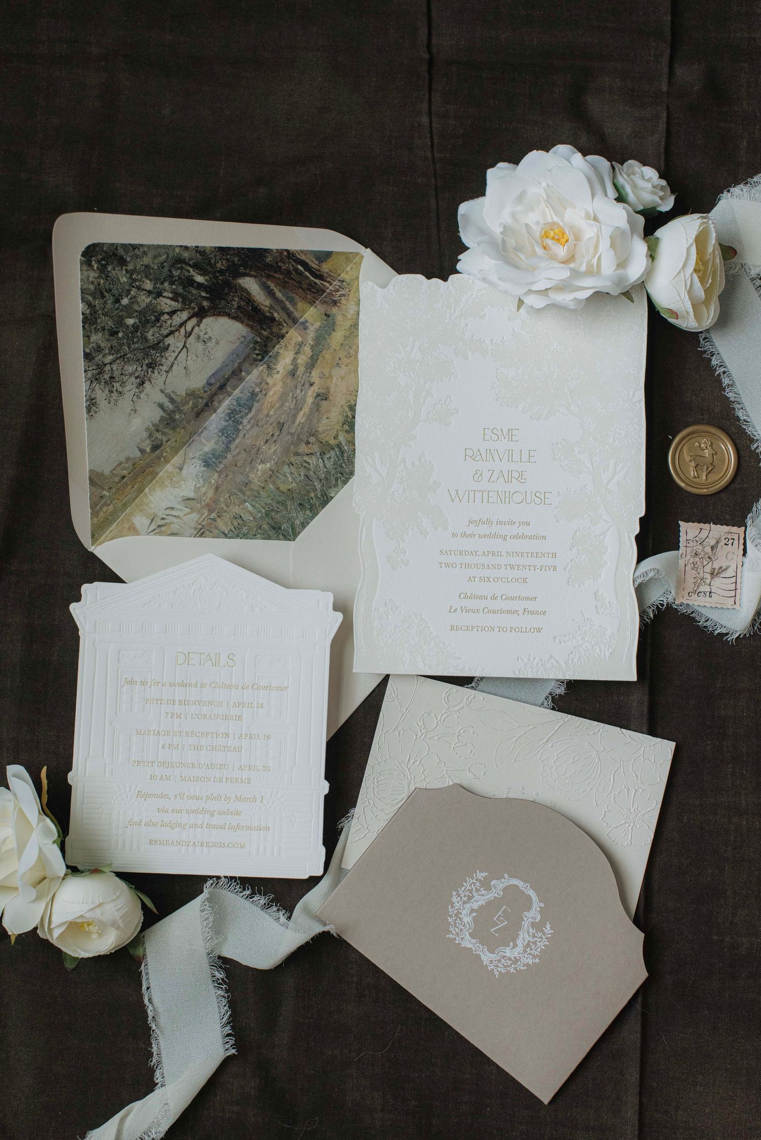Elegant wedding invitation suite with white floral details and taupe envelopes arranged on a dark background.