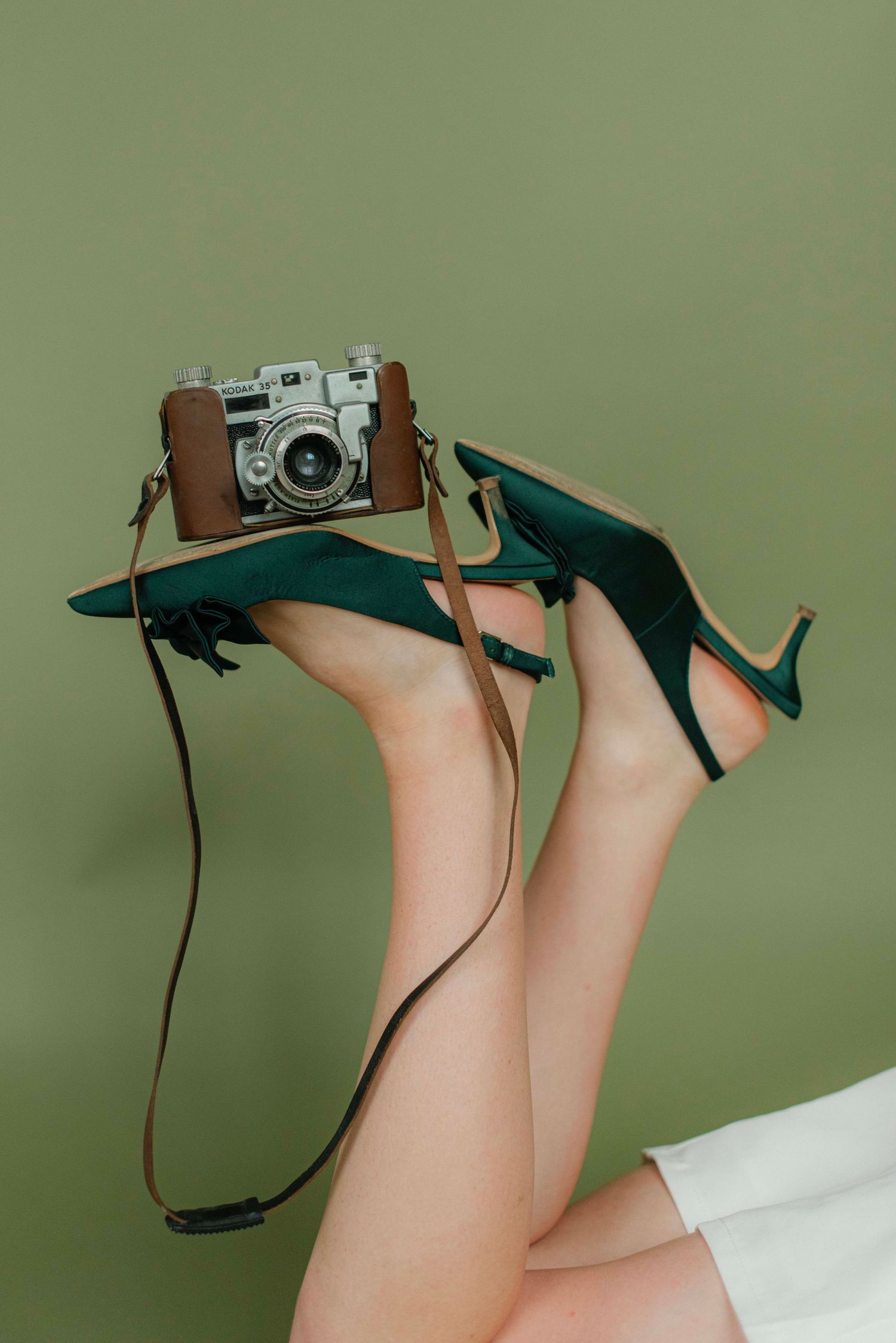 Artistic photo series of legs wearing green heels with a vintage camera against a green background.