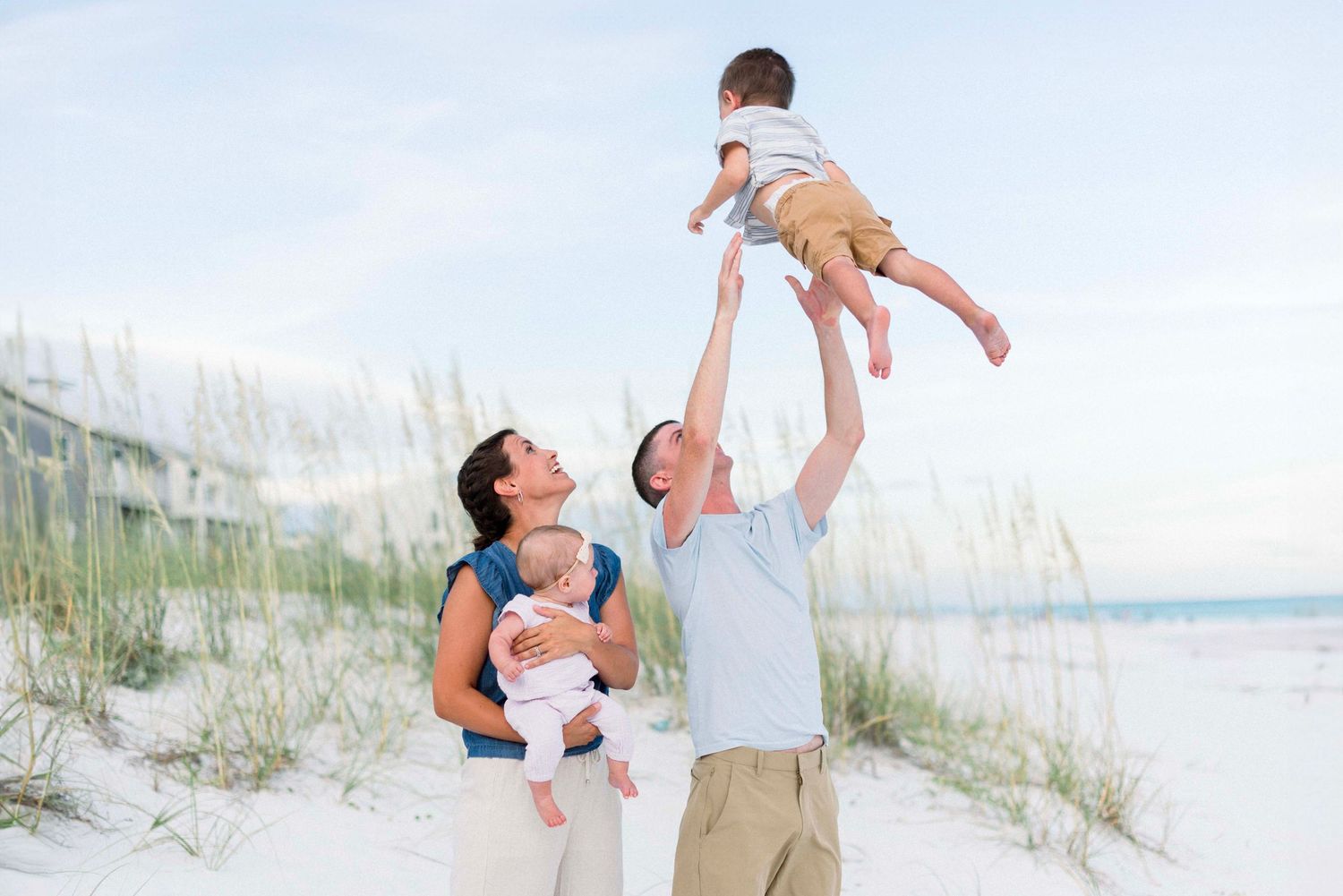 A family plays together on a sunny beach with sand dunes in the background.