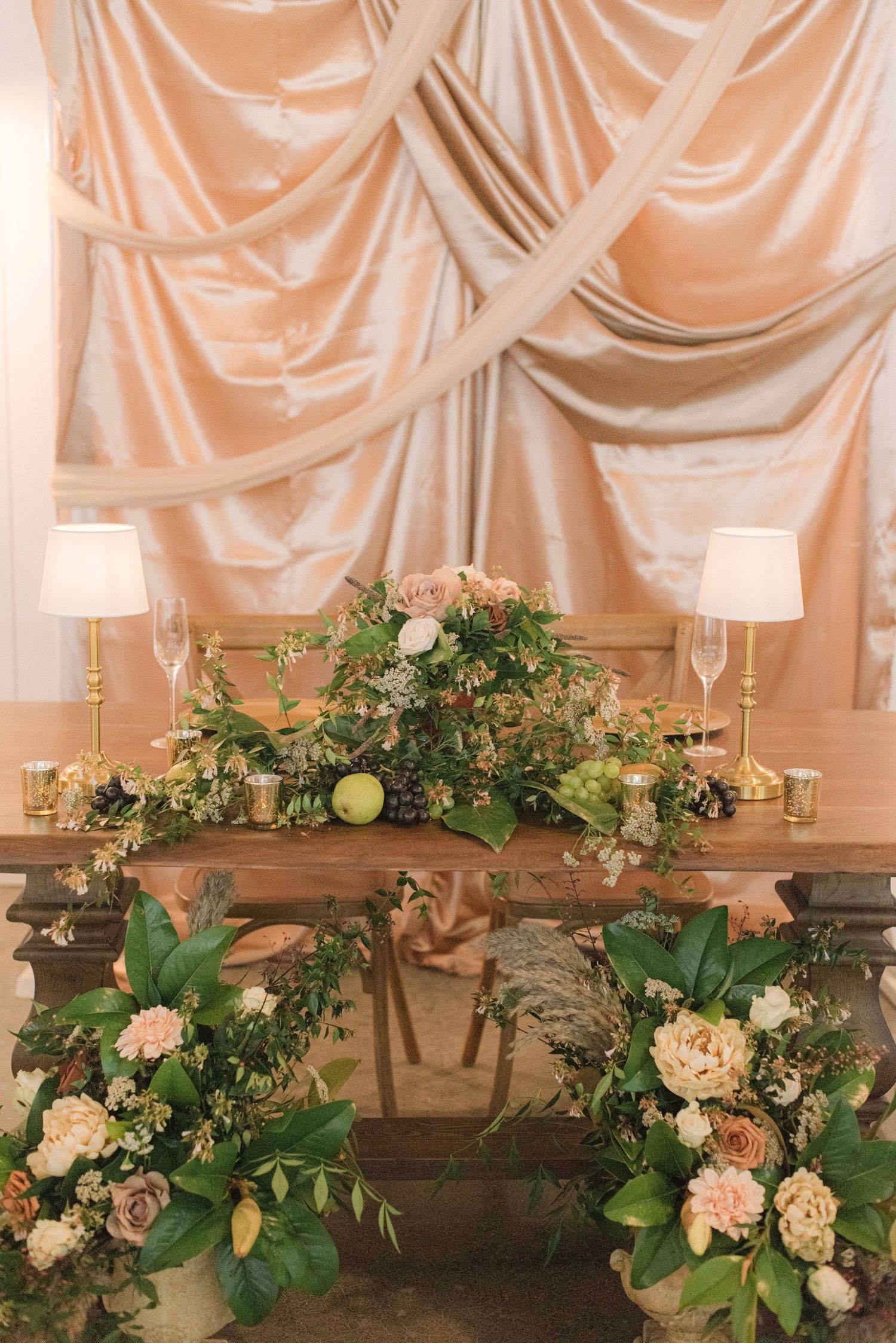 Elegant wedding decor features white candles and floral arrangements with greenery against draped fabric backdrop.
