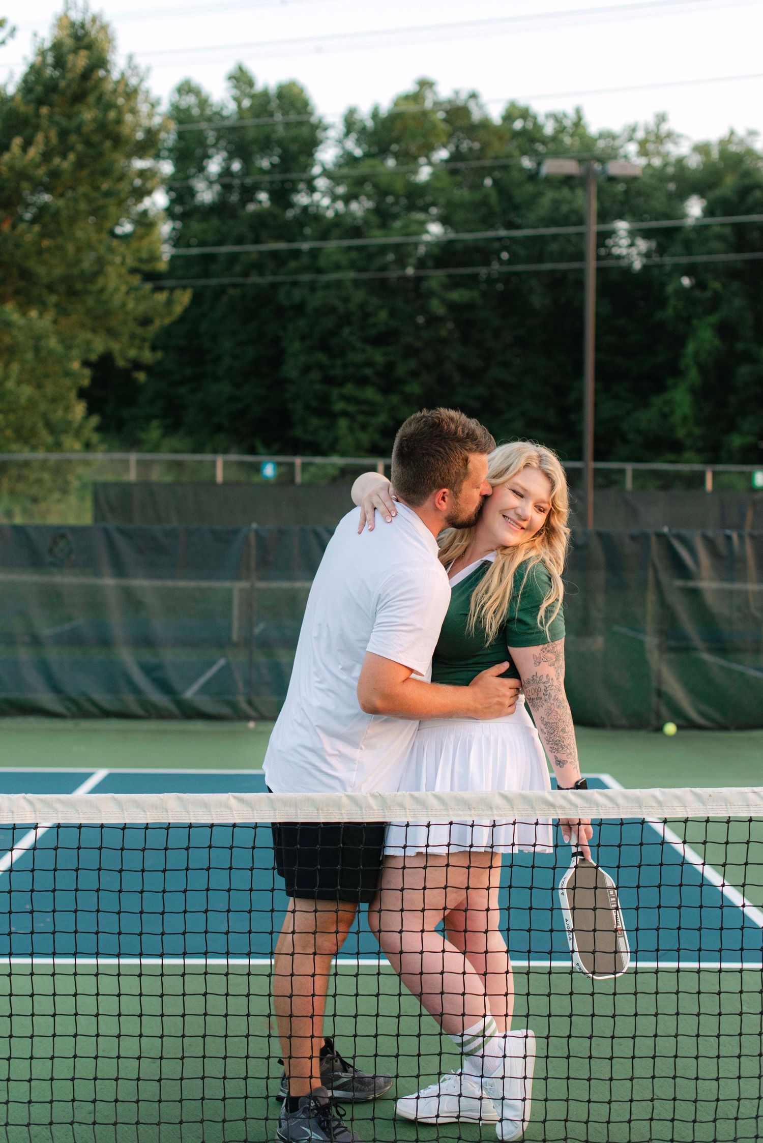 A couple embraces on a tennis court during a romantic photoshoot at sunset.