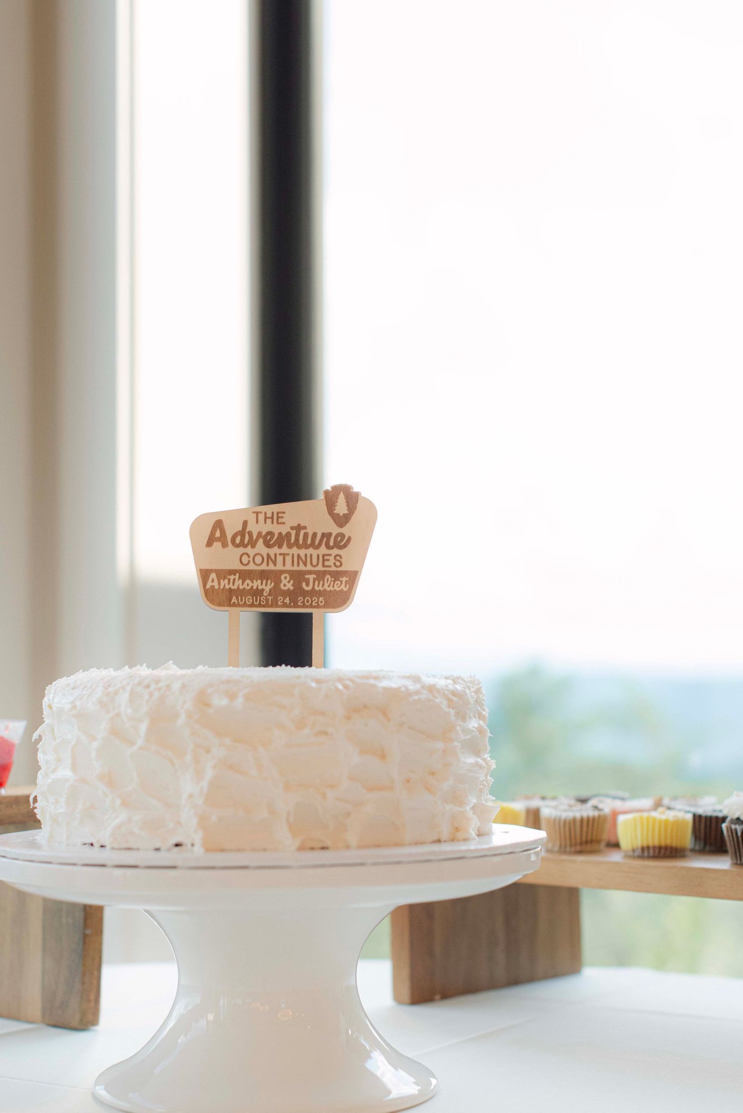 White wedding cakes displayed on stands with wooden adventure-themed toppers.