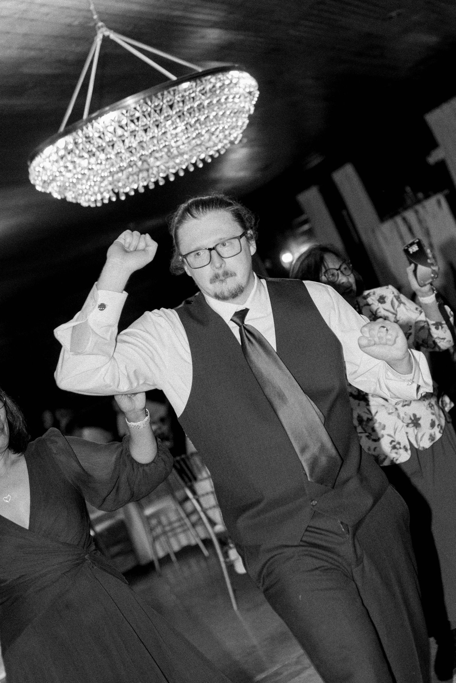 Black and white photos of wedding guests dancing under an elegant crystal chandelier.