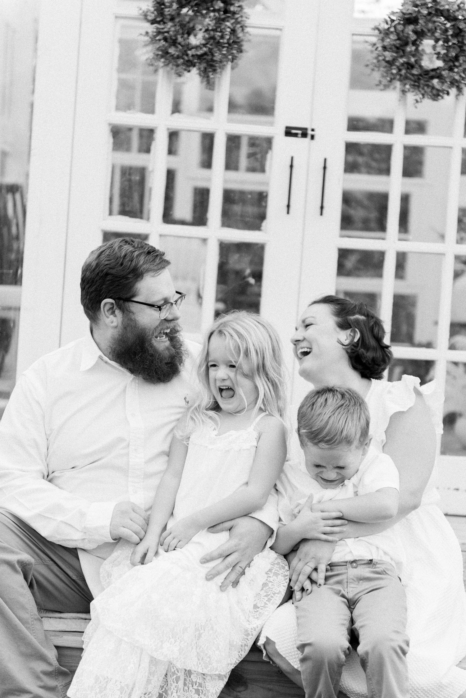 Family sharing candid laughs together on white furniture outdoors.