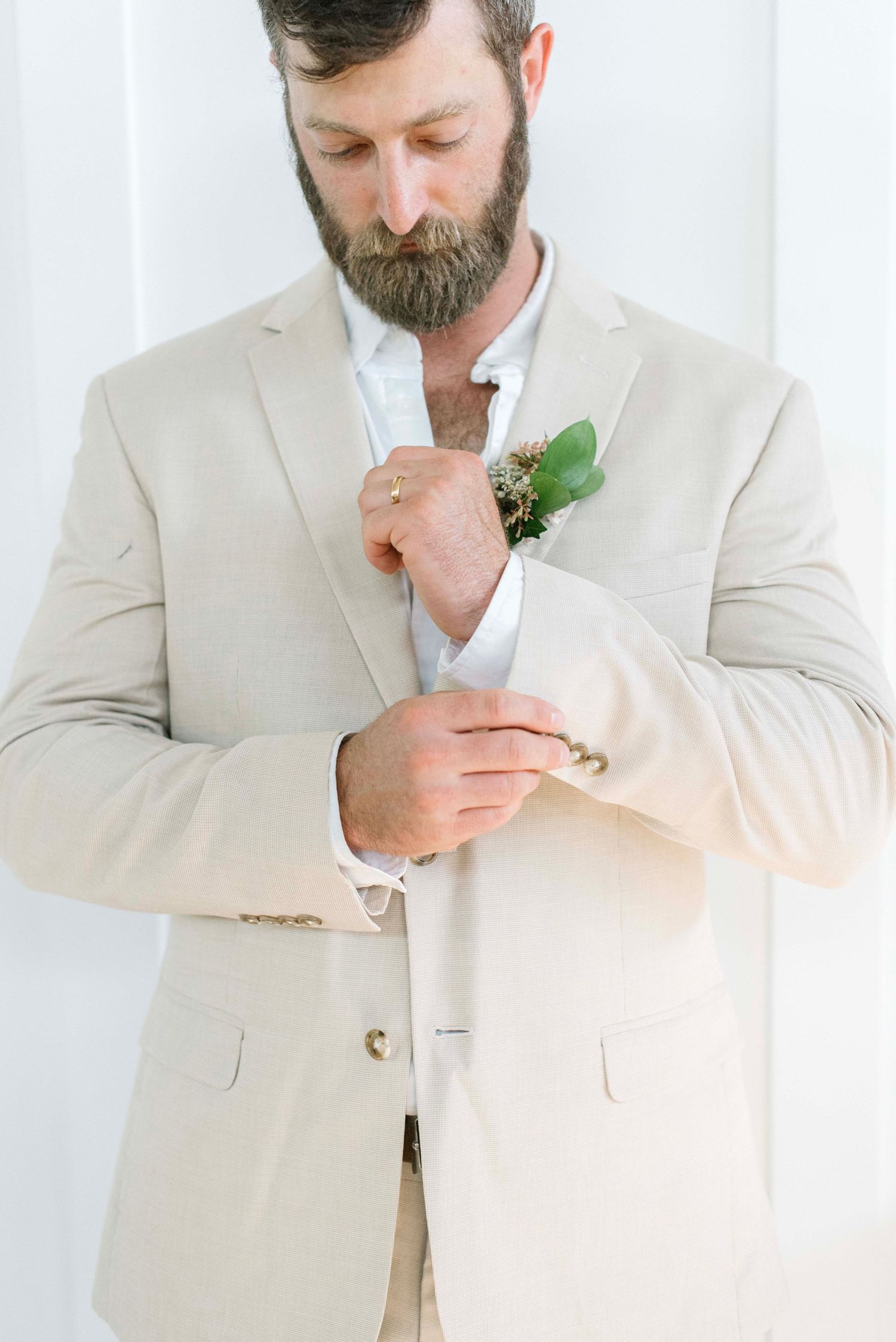 A series of photos showing a bearded person in a light colored suit adjusting their boutonniere.
