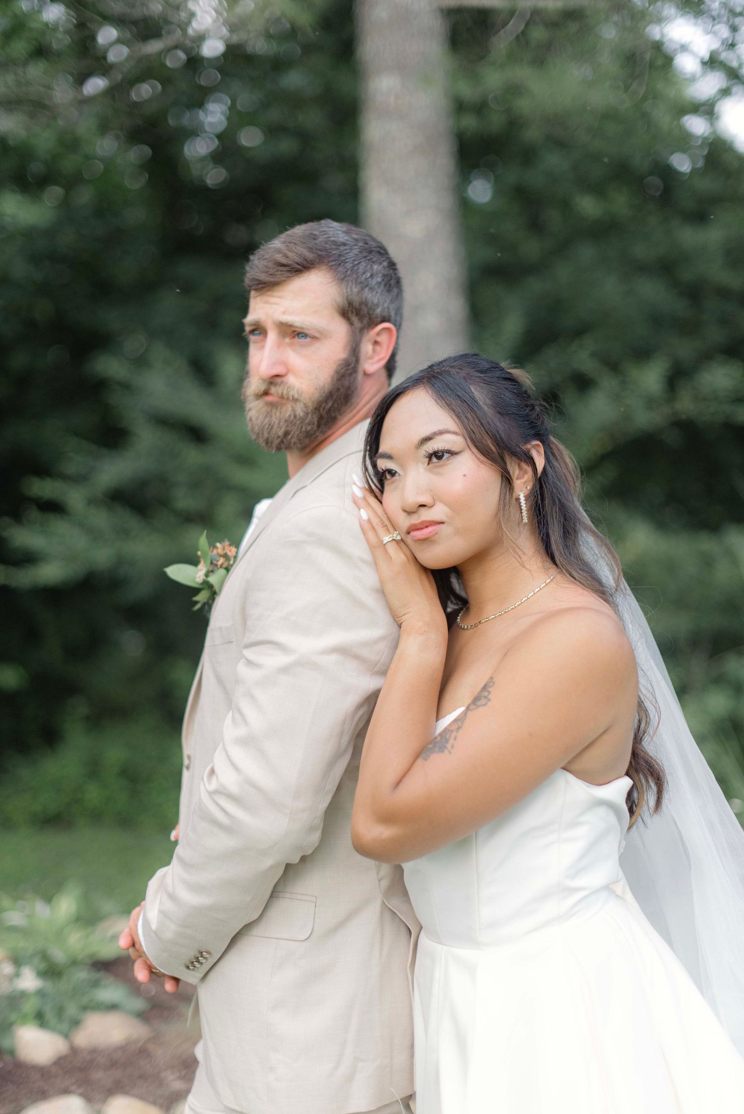 A bride and groom share a tender moment in a garden setting with trees in the background.