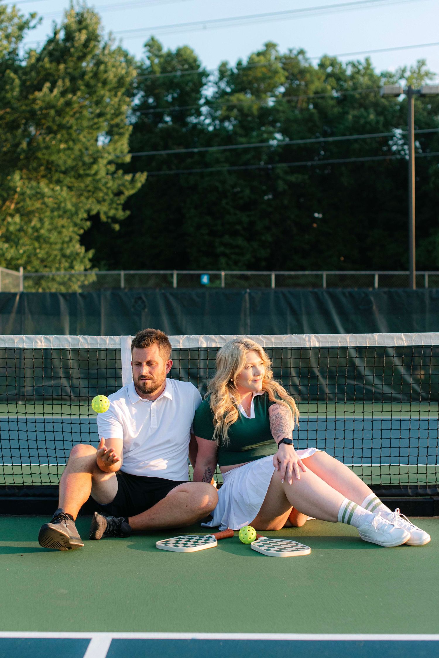 Two tennis players rest and laugh together while lying on a tennis court during a playful moment.