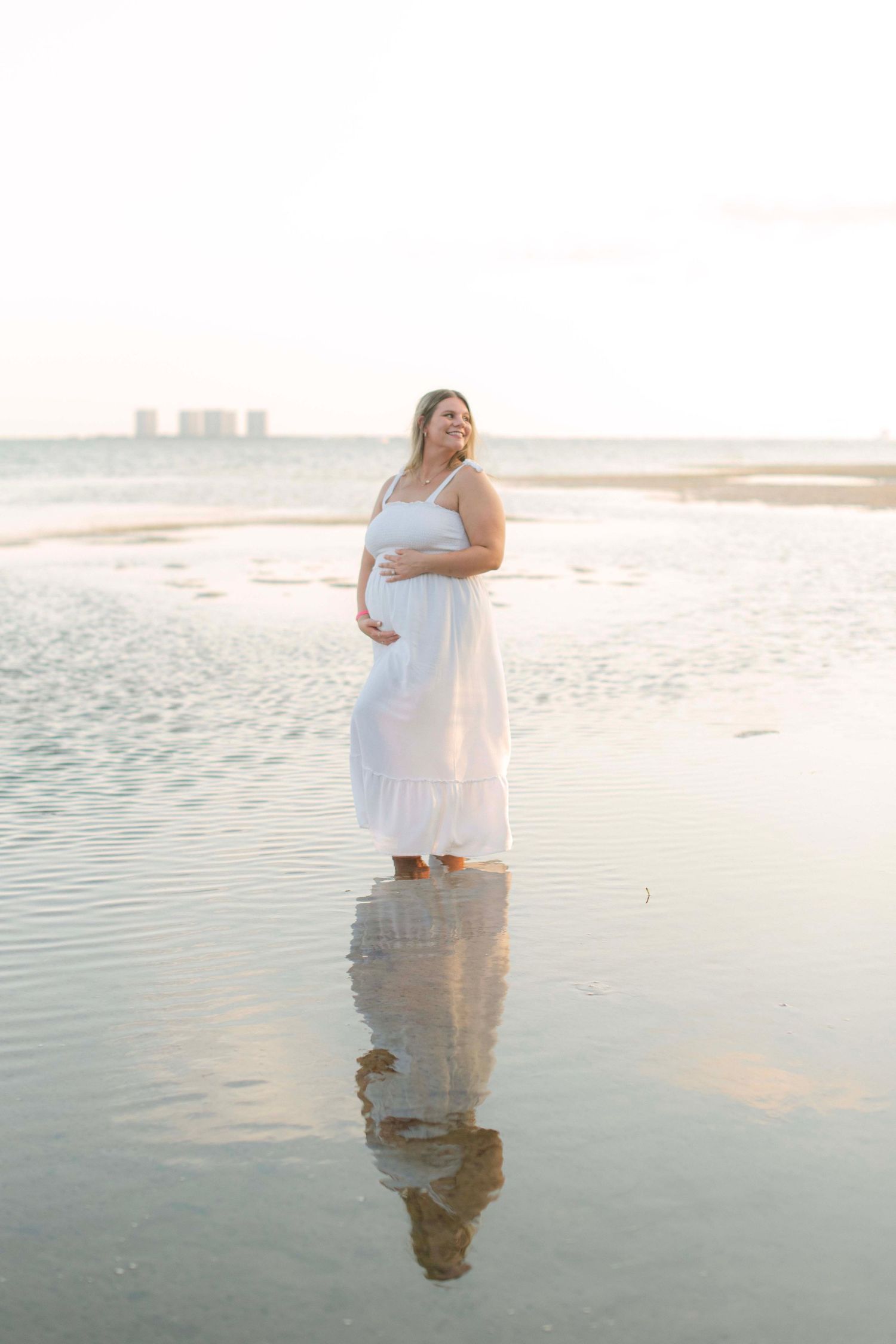 Two people stand in calm ocean waters during a dreamy sunset photoshoot.