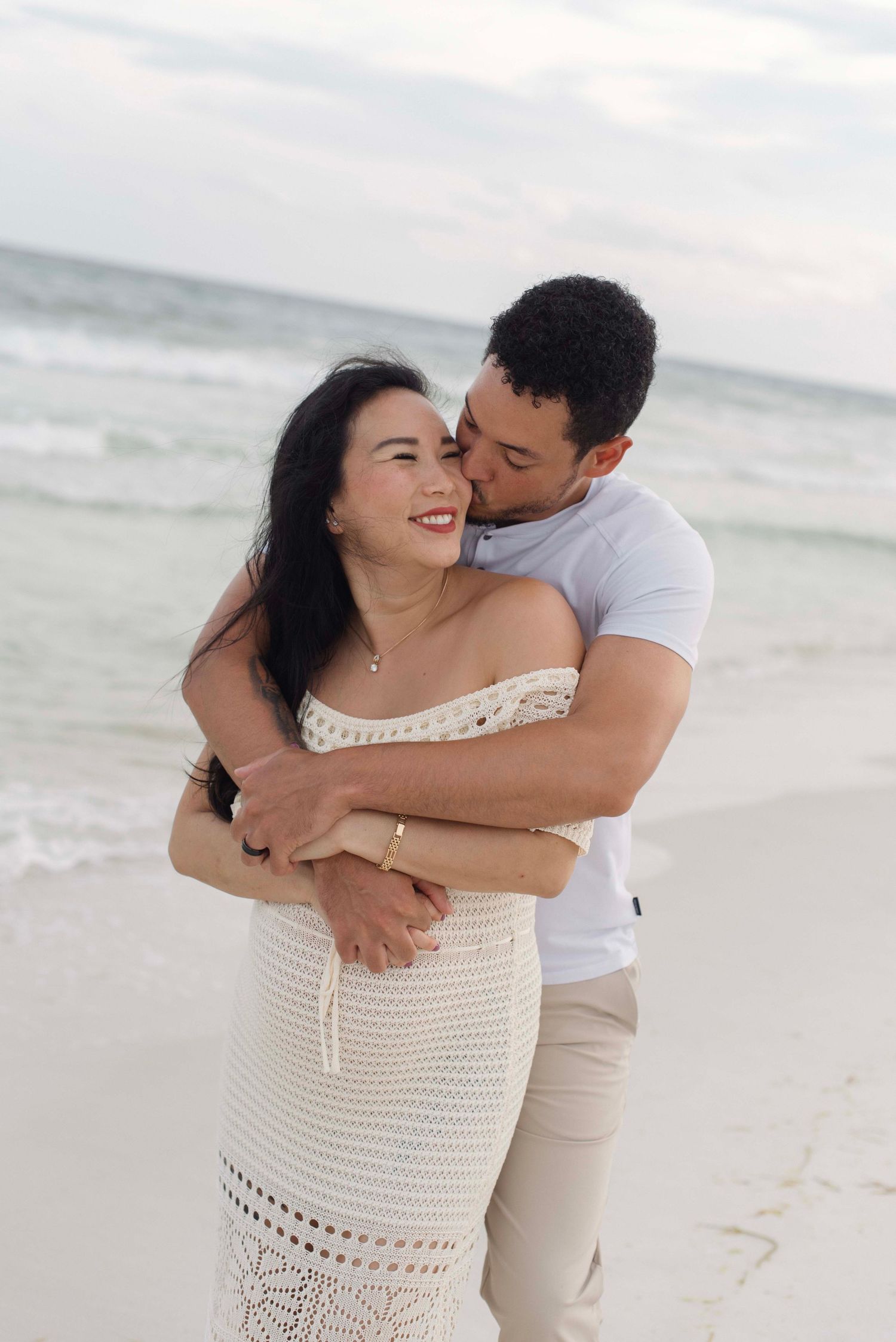 A couple embraces and laughs together during a romantic photoshoot on a sunny beach.