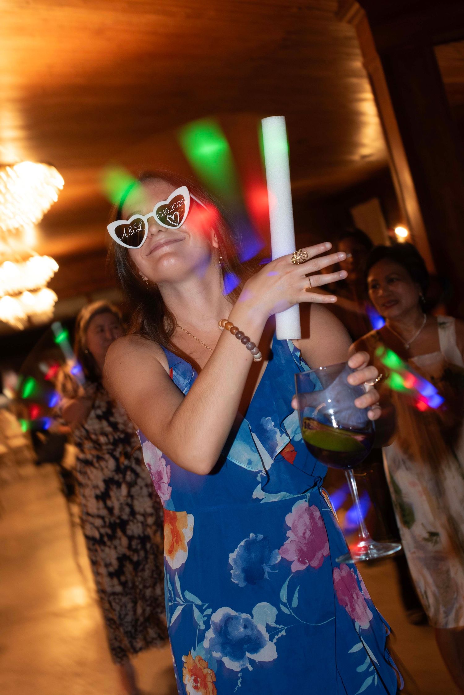 Wedding guests dancing at reception with colorful party lights in the background.