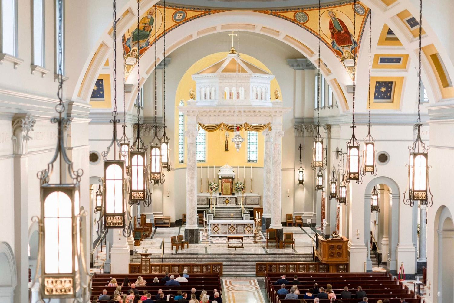 Interior view of a historic Catholic church with ornate arches, columns and a grand altar in white and gold tones.