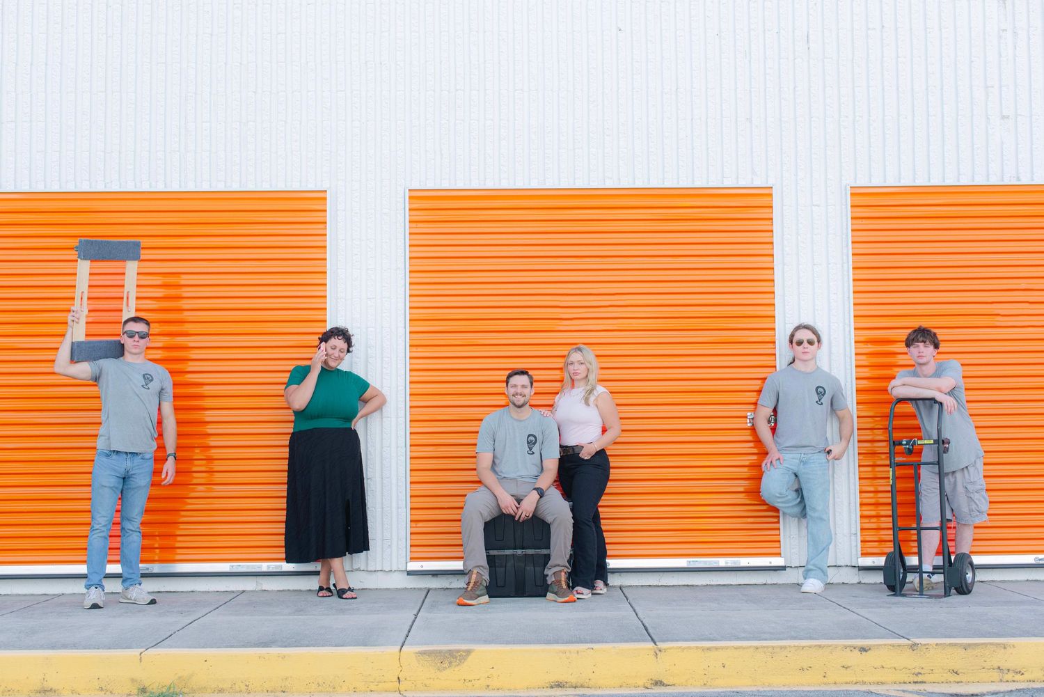 People sitting along an orange wall creating a minimalist urban scene.