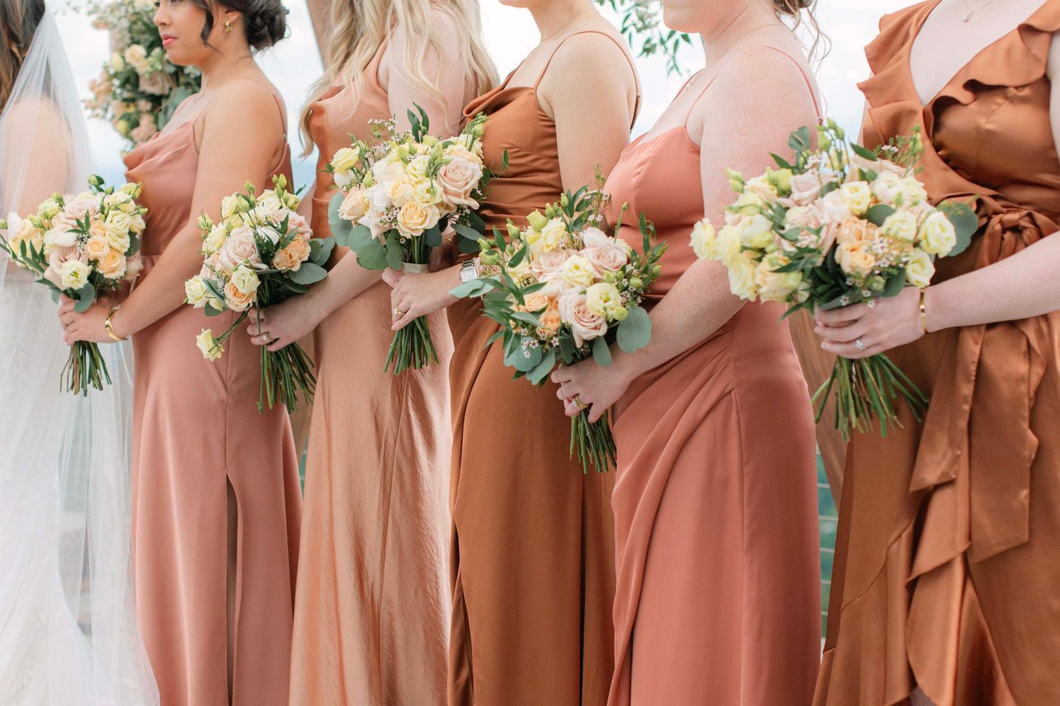 Bridesmaids in matching peach dresses hold elegant white and yellow floral bouquets.