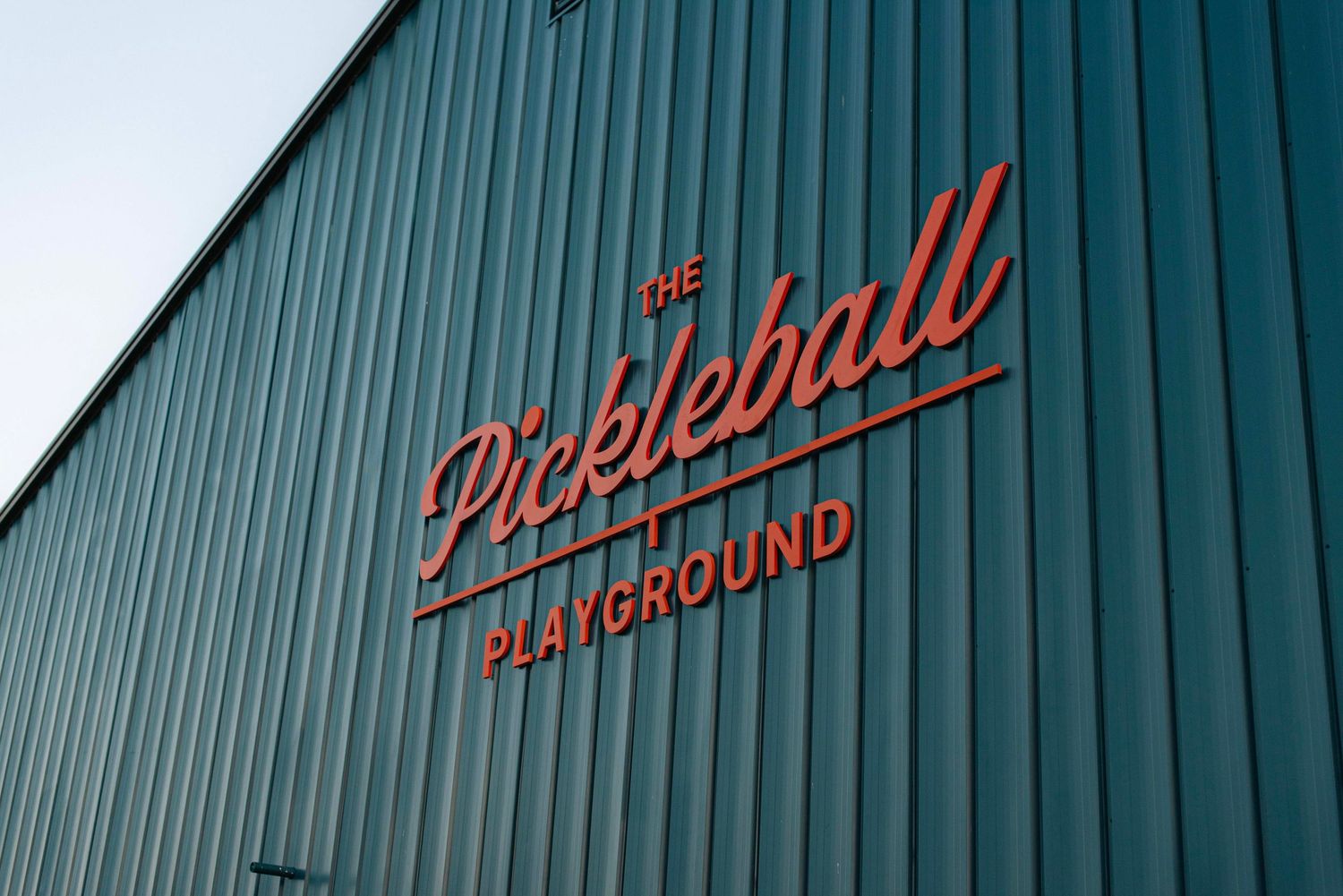 Green corrugated metal wall with partial red text signage visible against industrial building exterior.